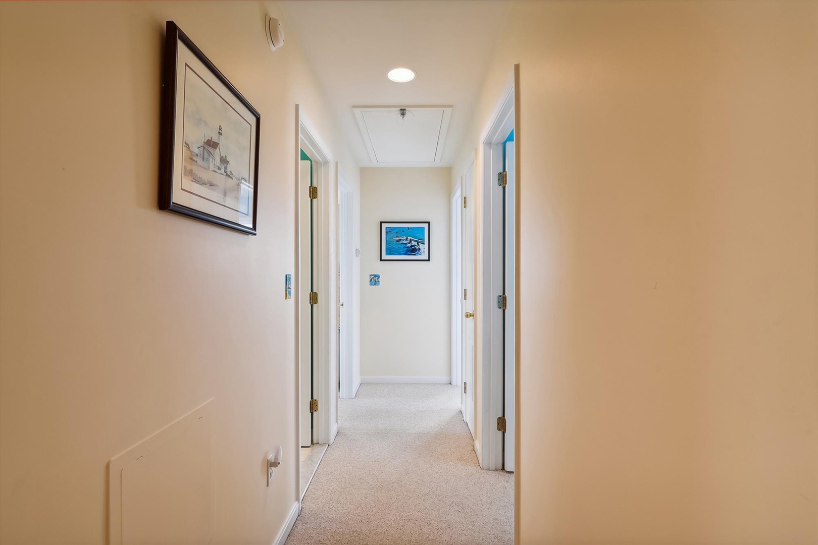 A bright, welcoming hallway with coastal artwork guides you to your private spaces, where soft carpeting and warm lighting create a cozy, home-away-from-home feel.