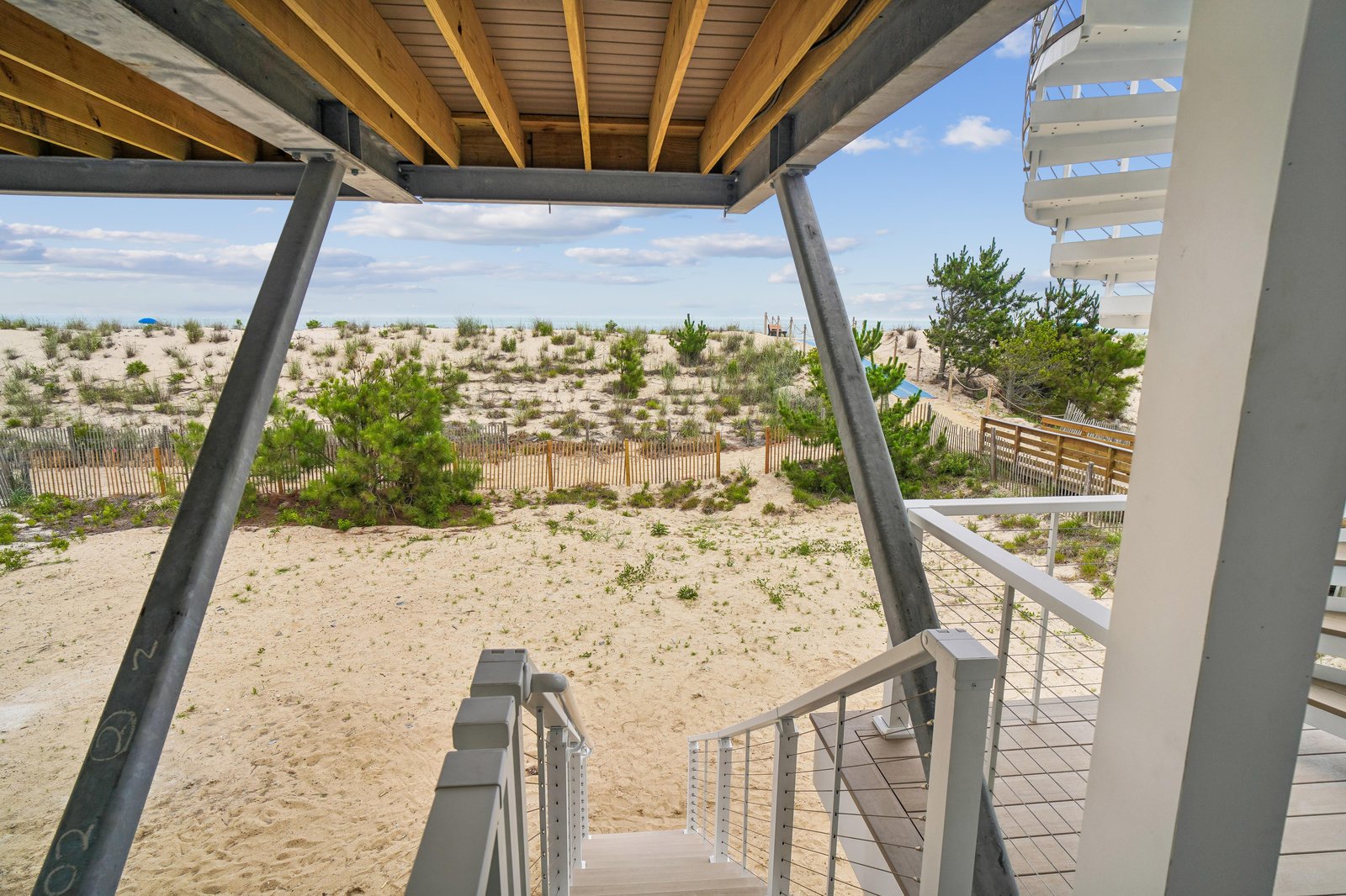 The property sits in a tranquil coastal landscape with sandy dunes, beach grasses, and natural vegetation stretching toward the horizon. A peaceful setting steps from the shore.