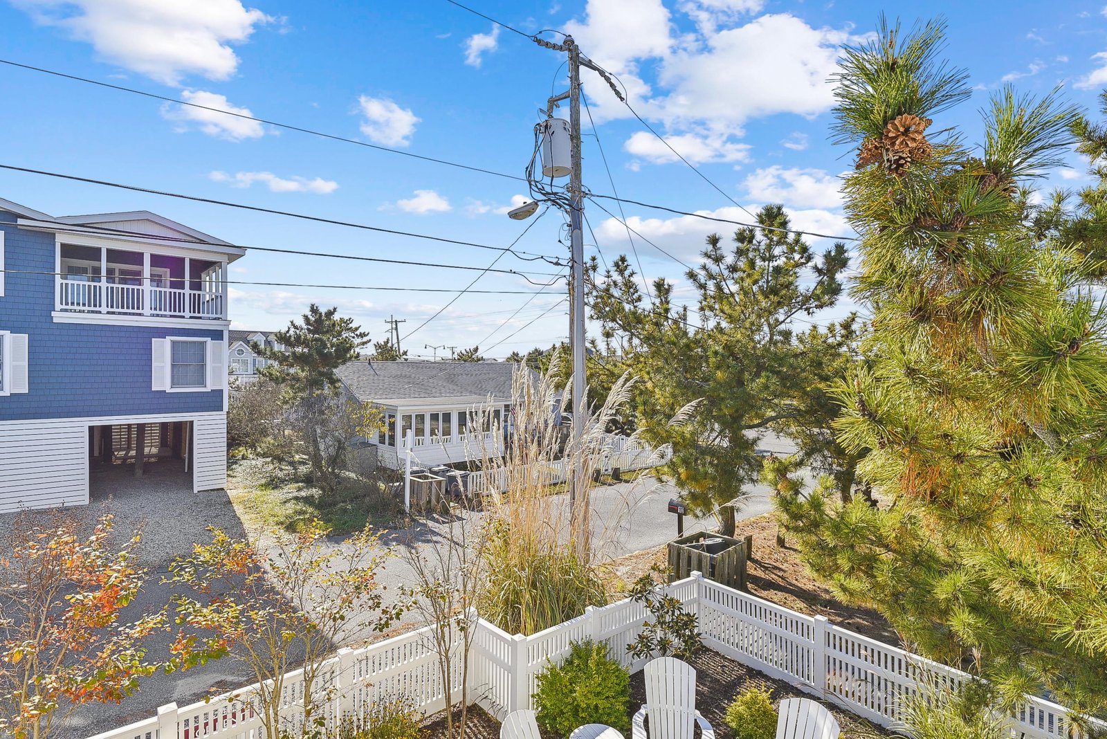 A peaceful coastal neighborhood with charming beach homes nestled among maritime pines and native greenery under a sunny blue sky.