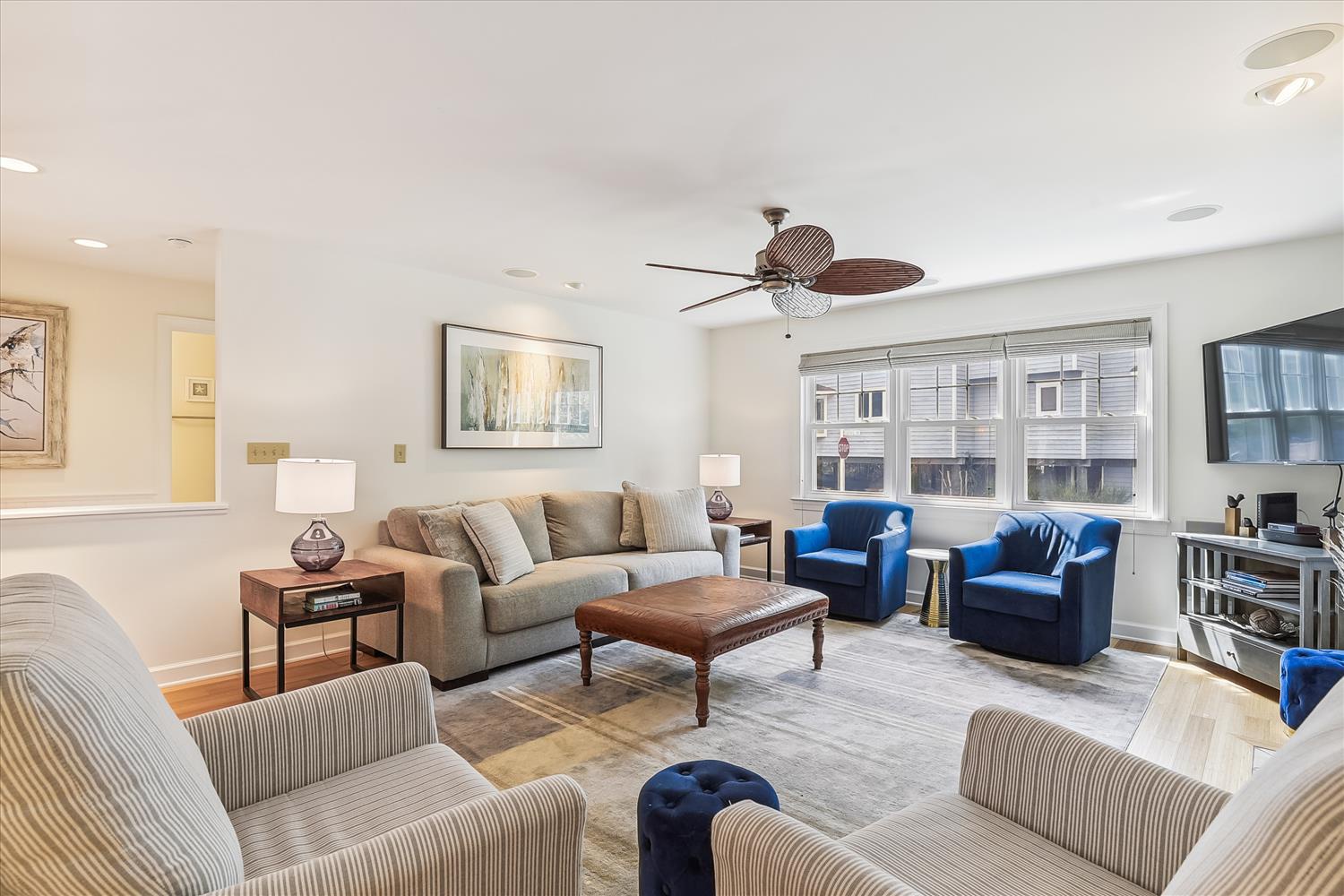 Step into your inviting living space, where plush seating, warm wood tones, and pops of blue create a perfect retreat. Sunlight streams through large windows, and the ceiling fan keeps you comfortable year-round.
