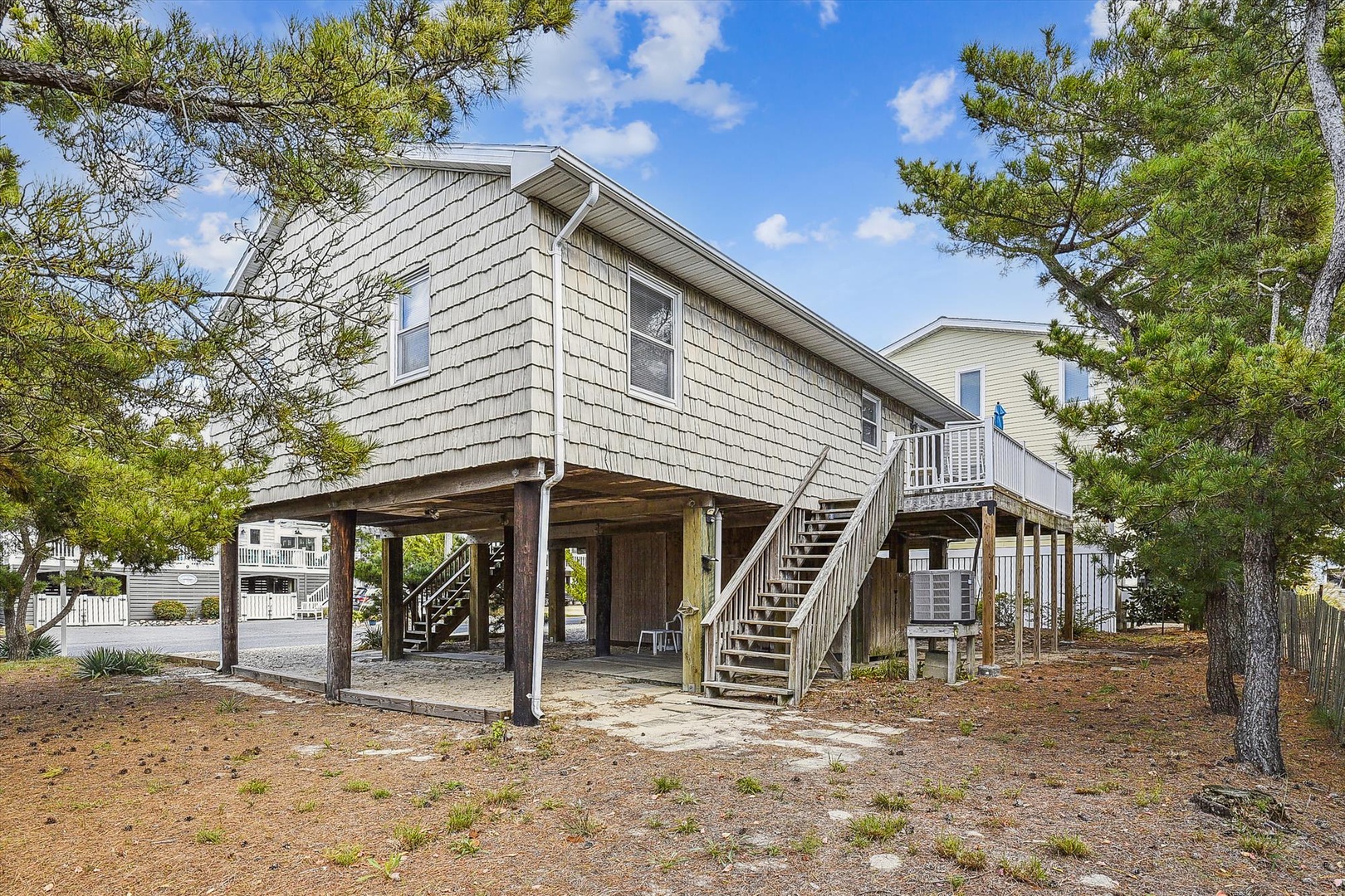 This coastal retreat features elevated construction with convenient ground-level parking, outdoor seating areas, and stairs leading to your private entrance—all nestled among mature pines in a peaceful neighborhood.