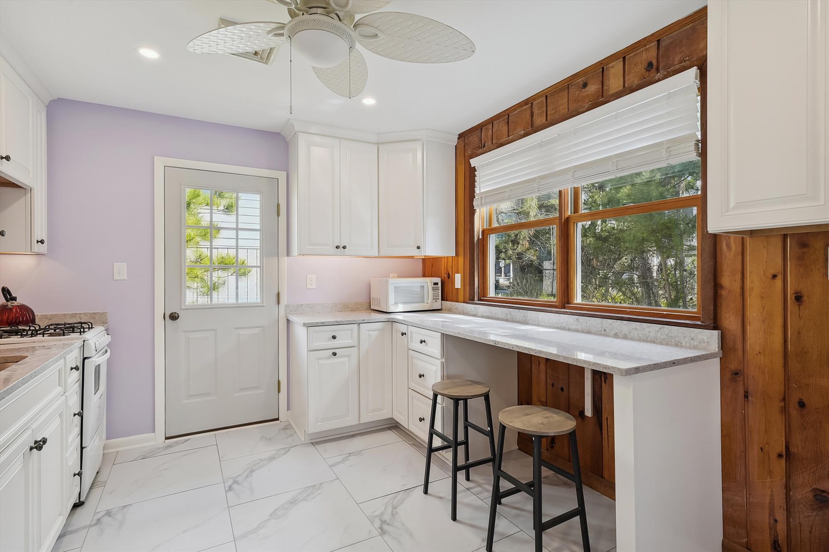 Your fully equipped kitchen blends coastal charm with modern convenience. Natural light pours through the window, illuminating marble-style counters and white cabinetry, while warm wood accents add character to your cooking space.