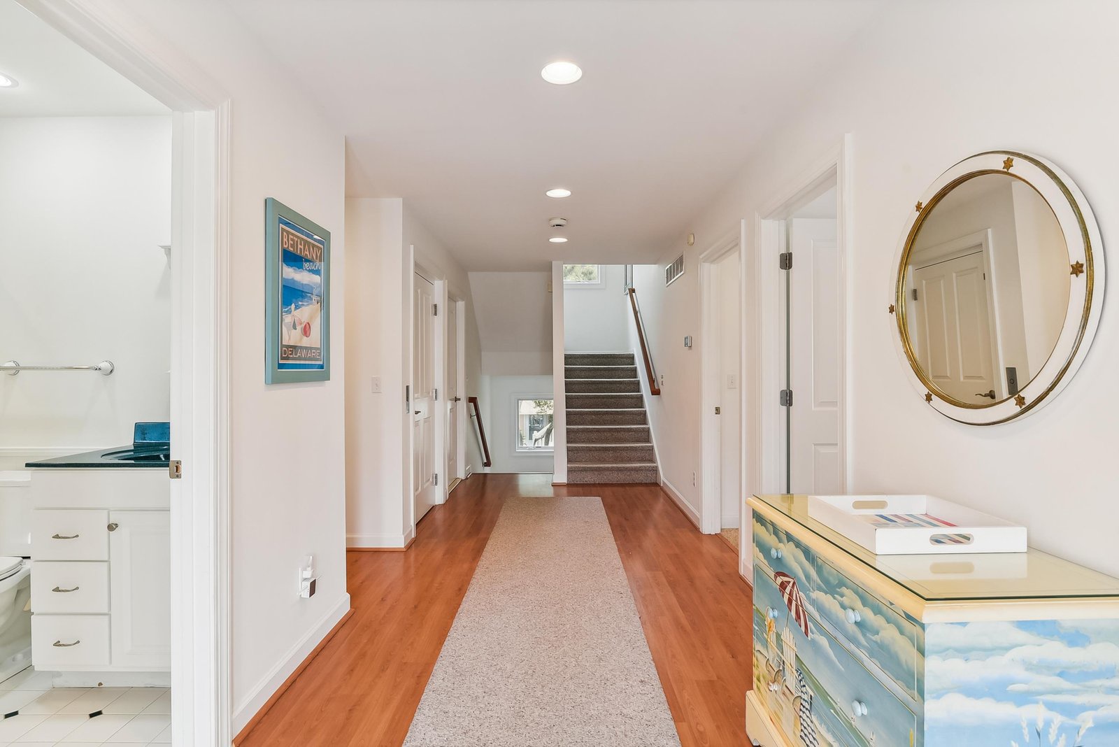 Bright, inviting entry hallway with warm wood floors and coastal-inspired touches, including a charming hand-painted chest beneath a gold-framed mirror. Step inside and feel instantly at home.
