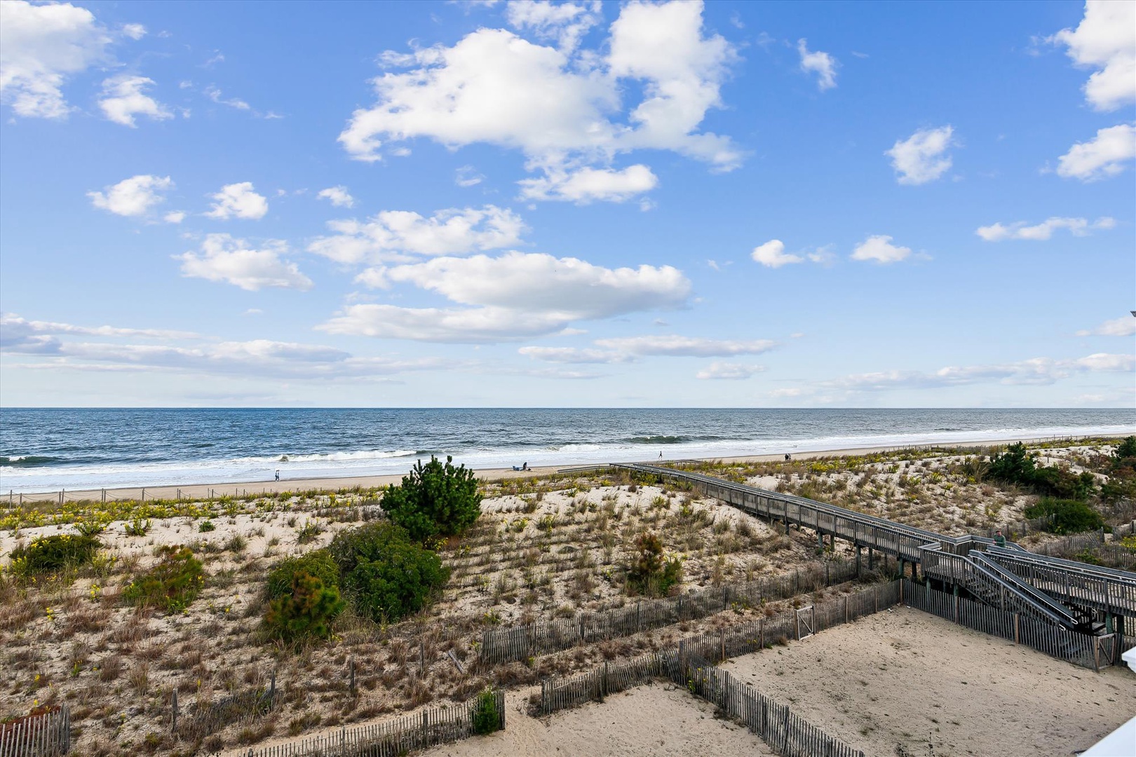 Scenic coastal pathway leads through dunes to a pristine sandy beach where gentle waves meet the shore under open blue skies—an ideal location for seaside living.