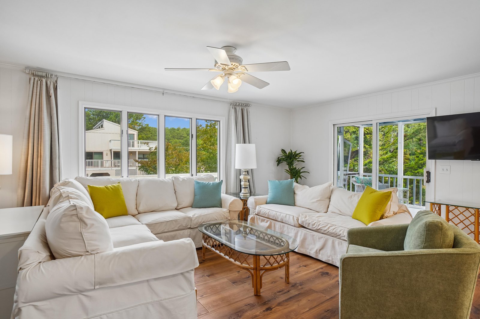 Unwind in this sunlit living room with plush seating and cheerful pops of color. Large windows frame leafy views, and a gentle ceiling fan keeps you cool while you relax indoors.