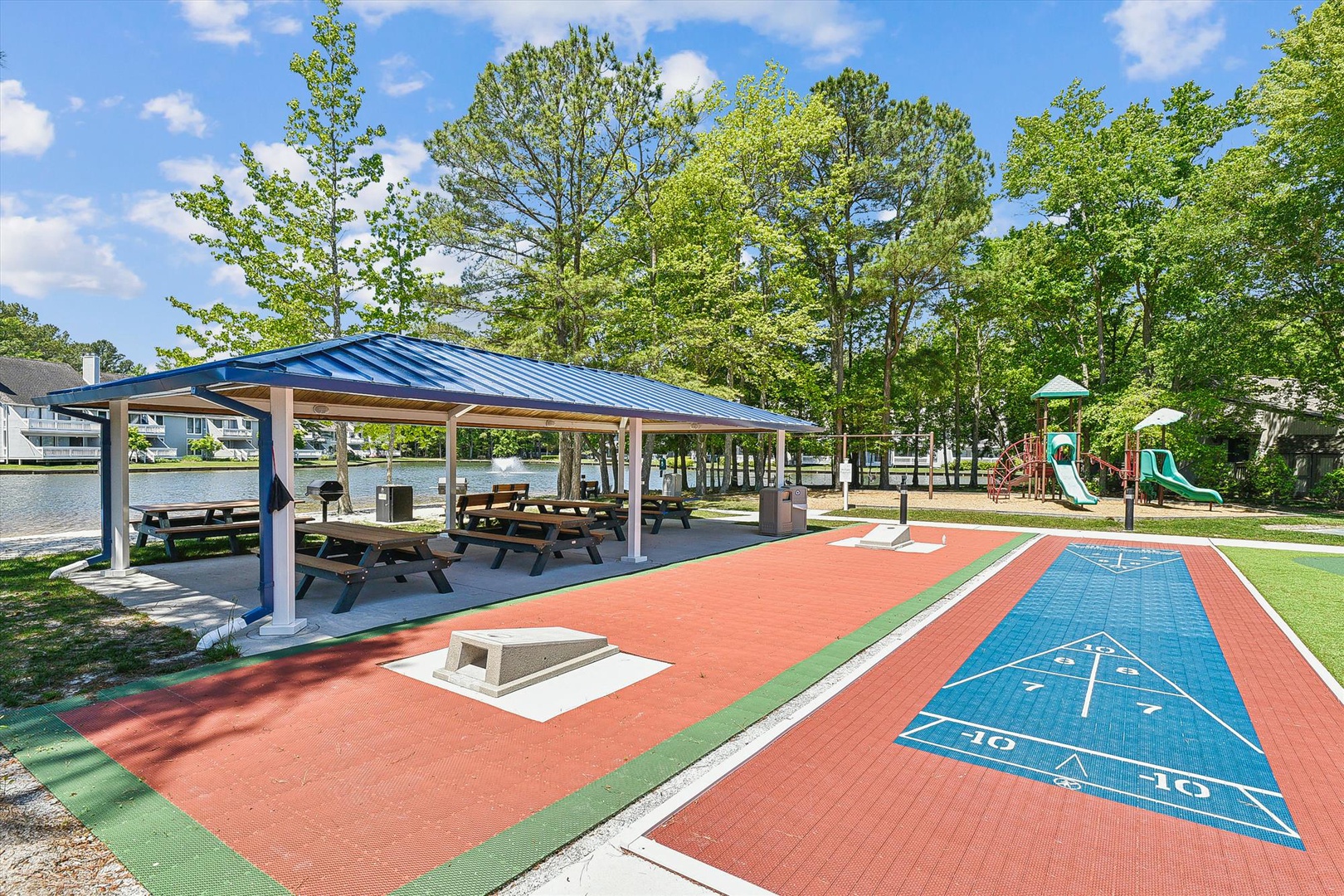 Lakeside recreational area features shuffleboard courts, covered picnic pavilion, playground, and expansive green space surrounded by mature trees—perfect for outdoor gatherings and family activities.