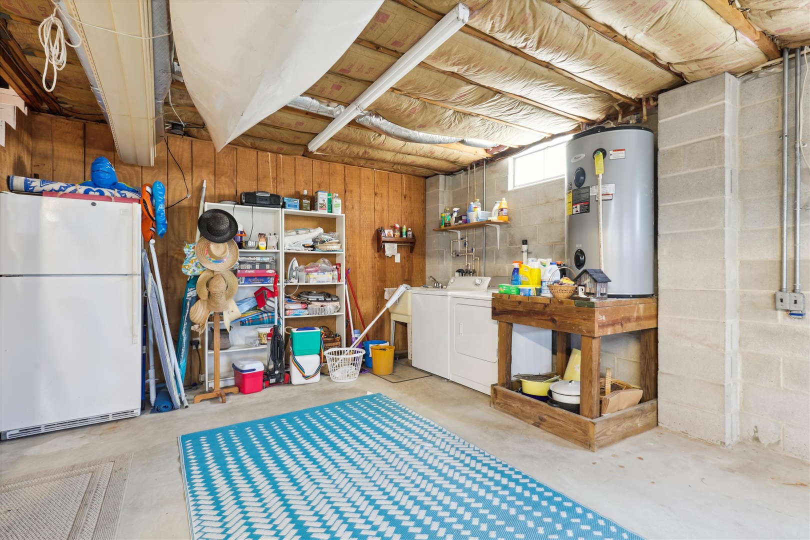 Basement utility area featuring organized storage, a refrigerator, sink, water heater, and exposed beam ceiling with insulation.