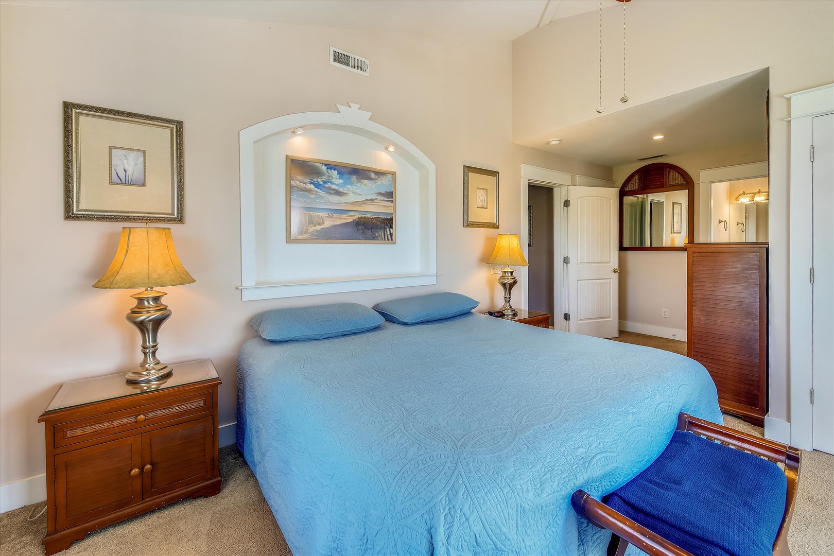 Settle into your peaceful retreat with soft linens, warm lighting, and thoughtful details—including a cozy bench for morning coffee and a built-in alcove framing serene coastal artwork above your plush bed.