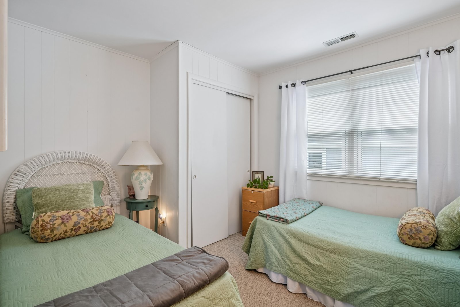 Two cozy beds dressed in soft sage linens invite restful nights, while natural light filters through bright windows. Your peaceful retreat awaits.