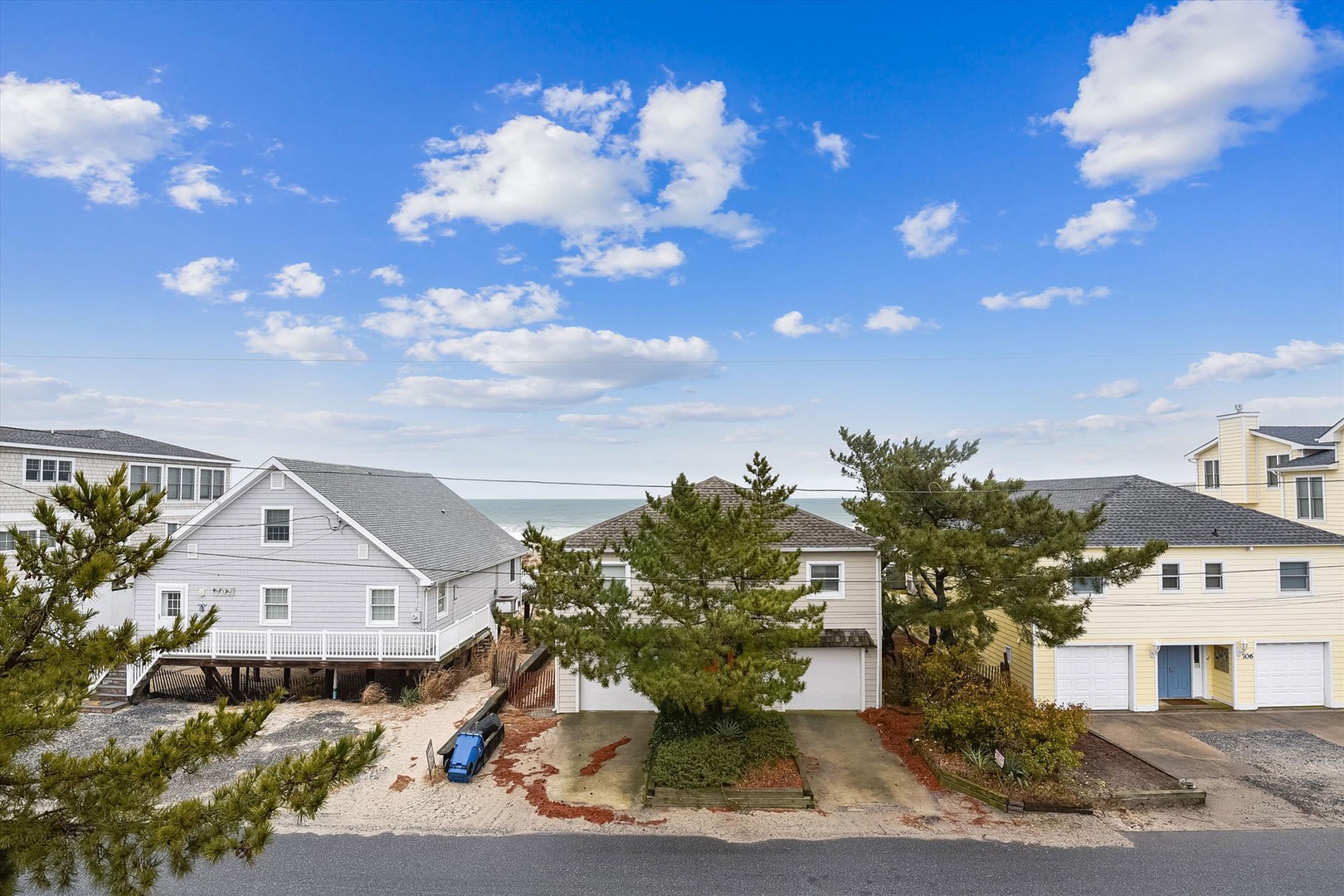 Coastal property nestled among beach homes with ocean views and direct access to sandy shores, surrounded by native pines and neighboring vacation residences.