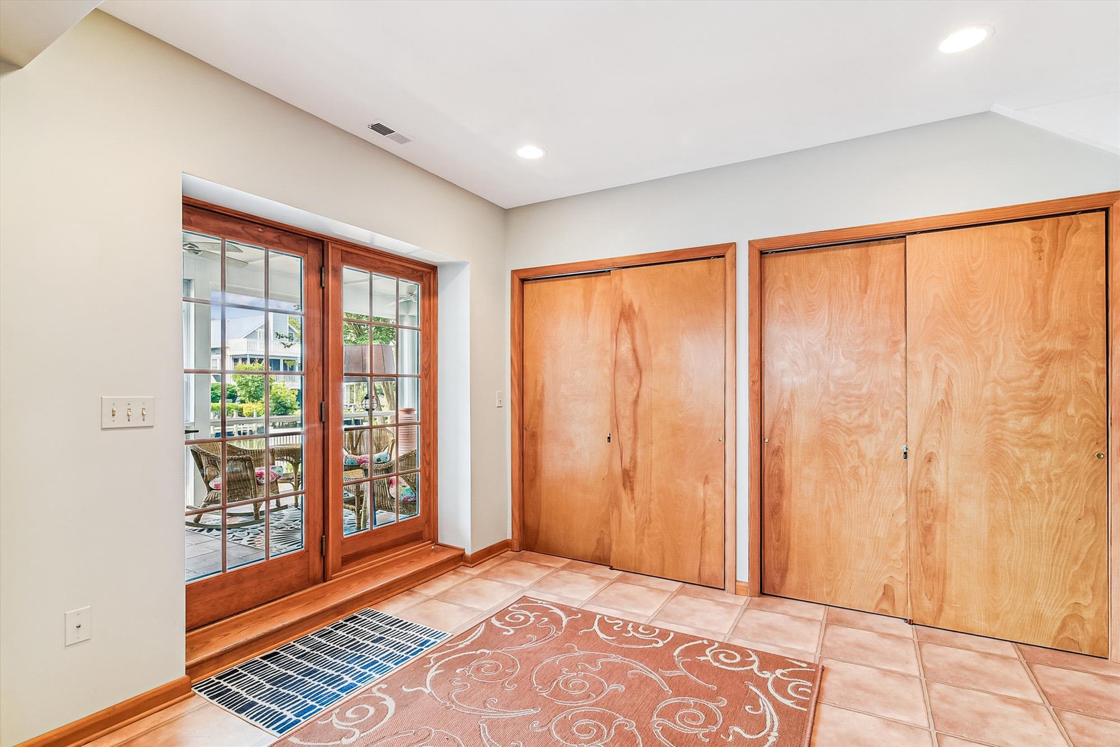Step into this bright, welcoming entryway with plenty of storage at your fingertips. The warm wood tones and tiled flooring invite you inside, while French doors open to your private outdoor patio.
