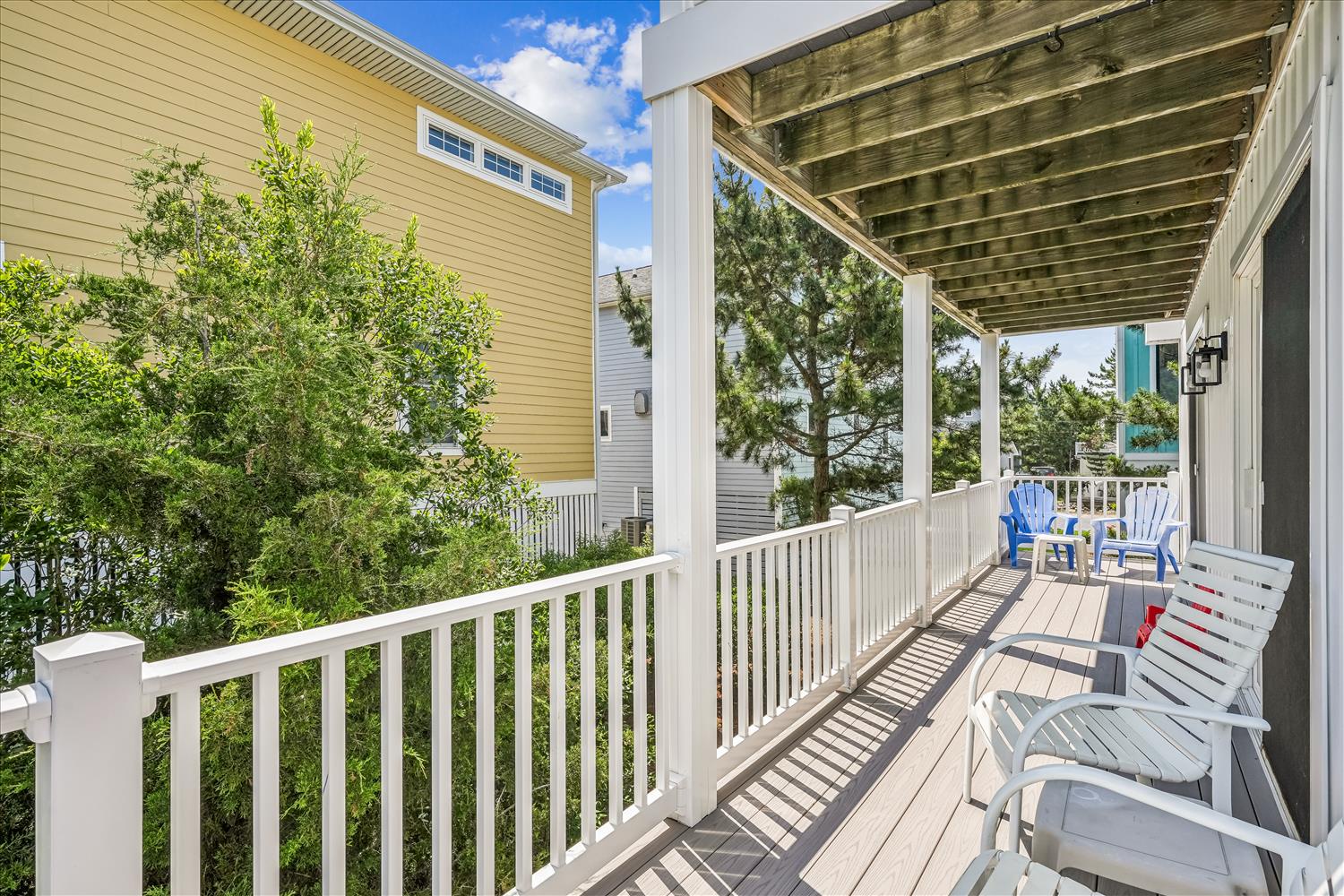 A spacious covered deck with lounge chairs offers a peaceful spot to relax outdoors, surrounded by greenery and featuring a glimpse of the water beyond.