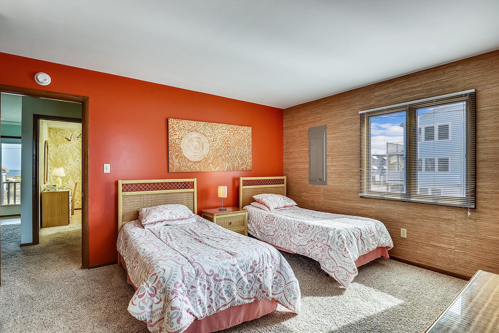 Your comfortable retreat features two twin beds with decorative linens, warm wood tones, and a vibrant orange accent wall that adds energy to your restful space.