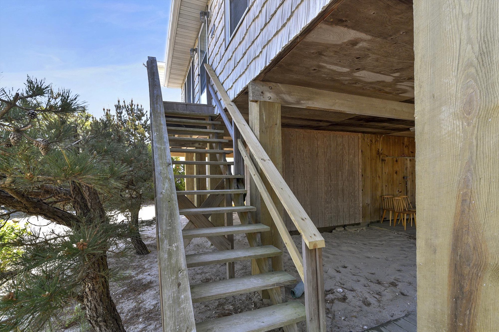 Coastal property features direct beach access with natural dune vegetation and wooden structures providing shaded outdoor space beneath the main building entrance.