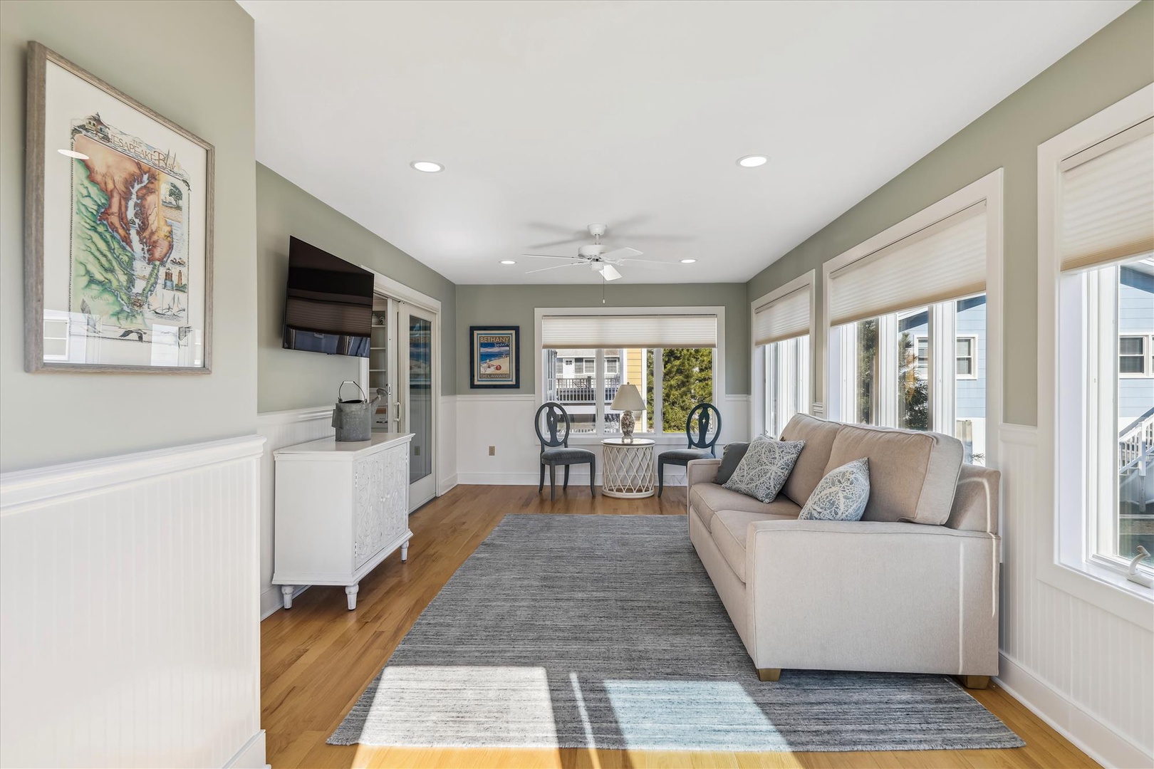 Step into your serene coastal retreat with soft sage walls, warm hardwood floors, and a plush sofa perfect for unwinding. Natural light pours through large windows, framing views of the neighborhood and creating a bright, welcoming space where relaxation 