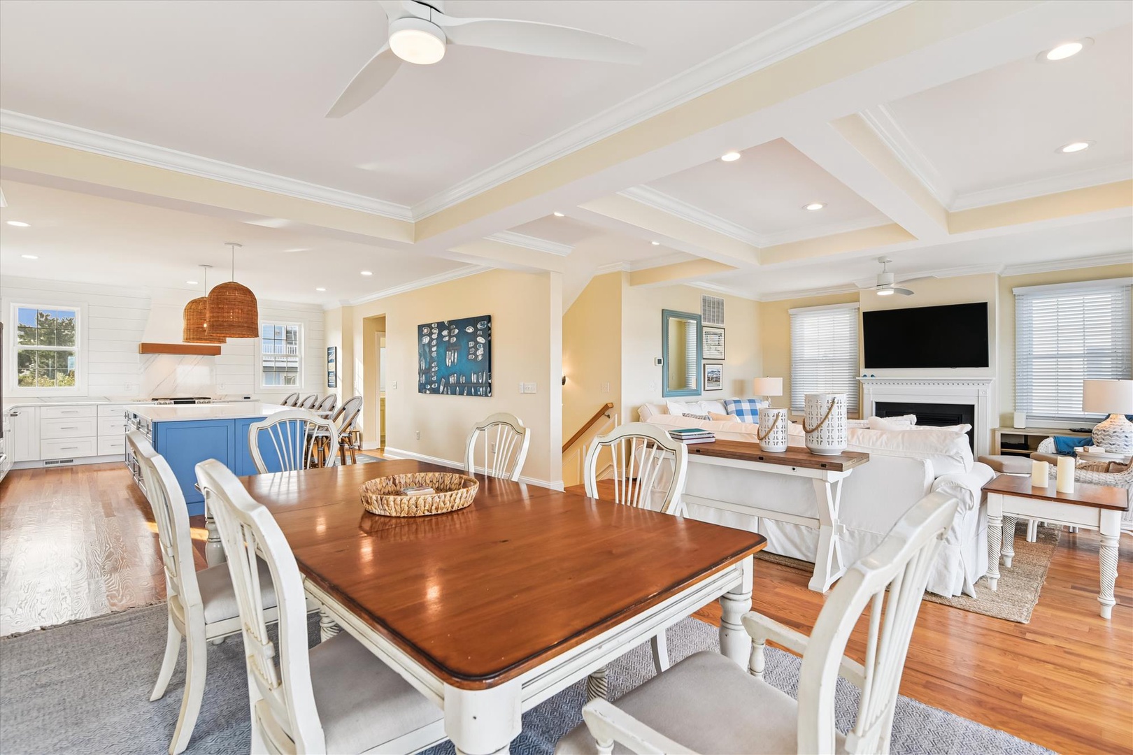 Gather around the warm wood dining table while the chef works in your spacious kitchen. Coastal charm fills this open-concept living space, perfect for family meals and relaxing evenings together.