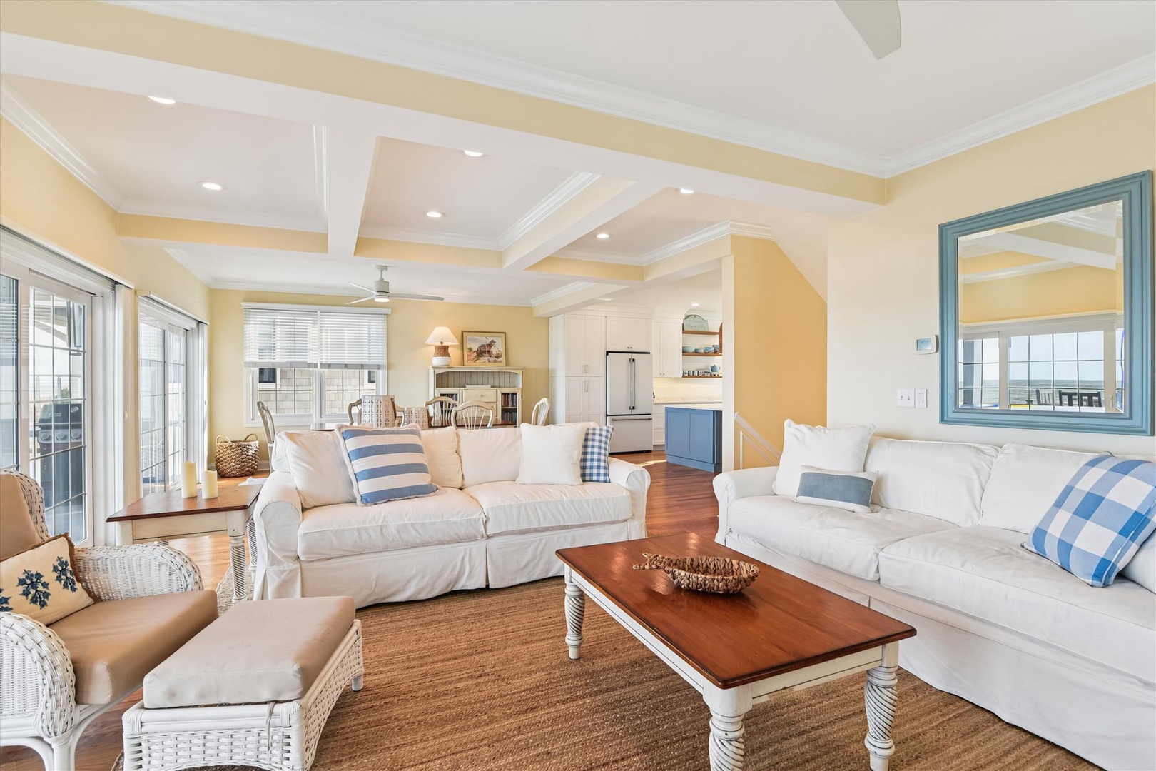 Sink into plush white sofas and enjoy the airy, sun-drenched open layout with coastal charm. Coffered ceilings and warm hardwood floors invite you to unwind in style.