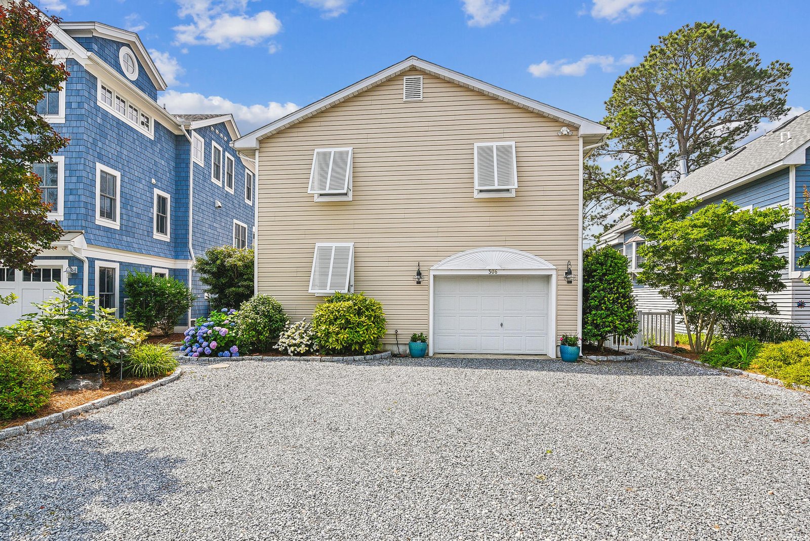A charming beach house with classic coastal architecture, framed by lush greenery and mature trees, featuring ample parking and a welcoming front entrance.