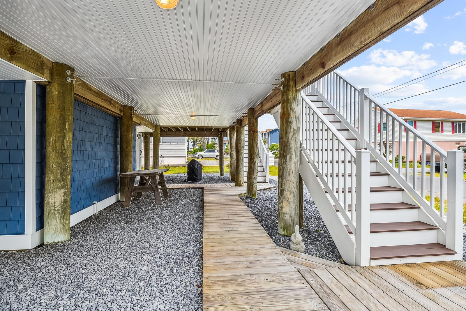 A spacious covered lower-level area with exterior access and stairway leading to the main home, featuring coastal architecture in a quiet beachside neighborhood.