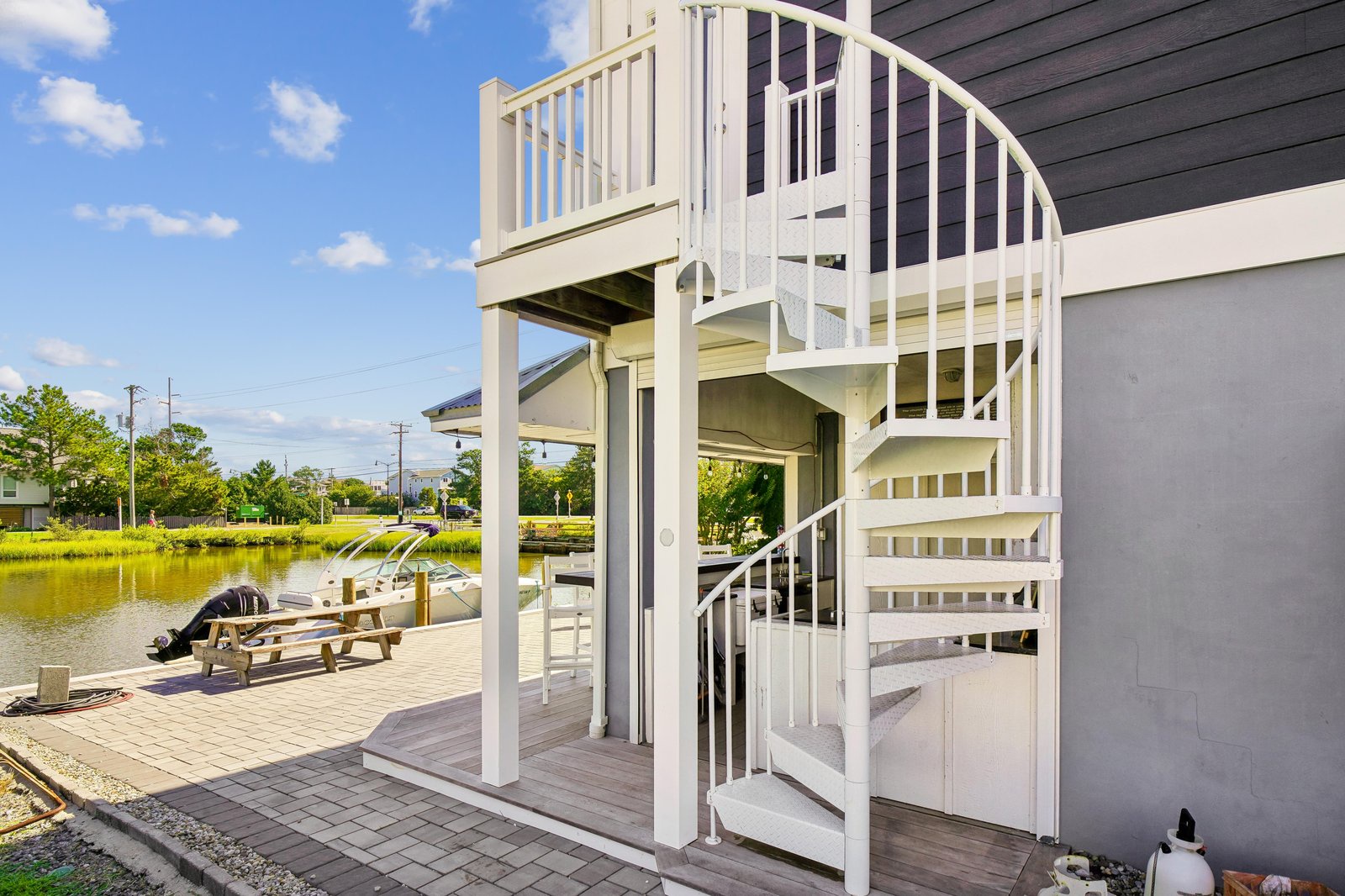 A spiral staircase connects your waterfront deck to an upper-level balcony, framing serene canal views and a shaded picnic spot where you can watch boats drift by.