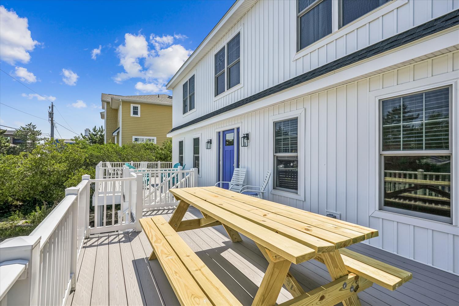 The modern white exterior features a private deck where you can gather around the new picnic table, perfect for meals under a bright blue sky.