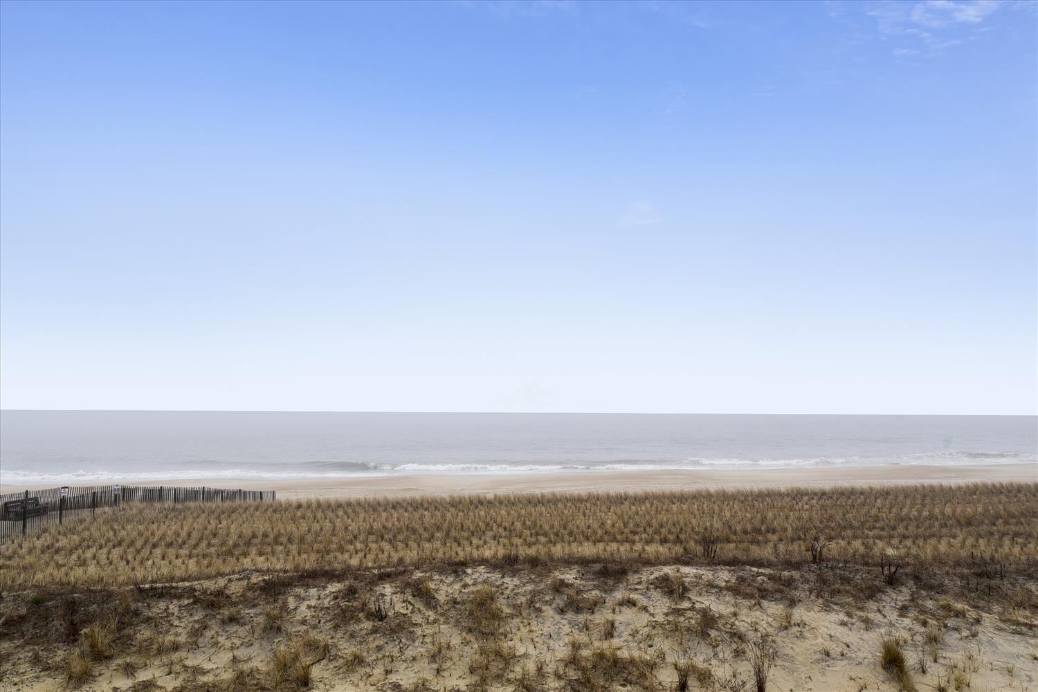 Expansive coastal vista with pristine beach stretching to the horizon under clear blue skies.