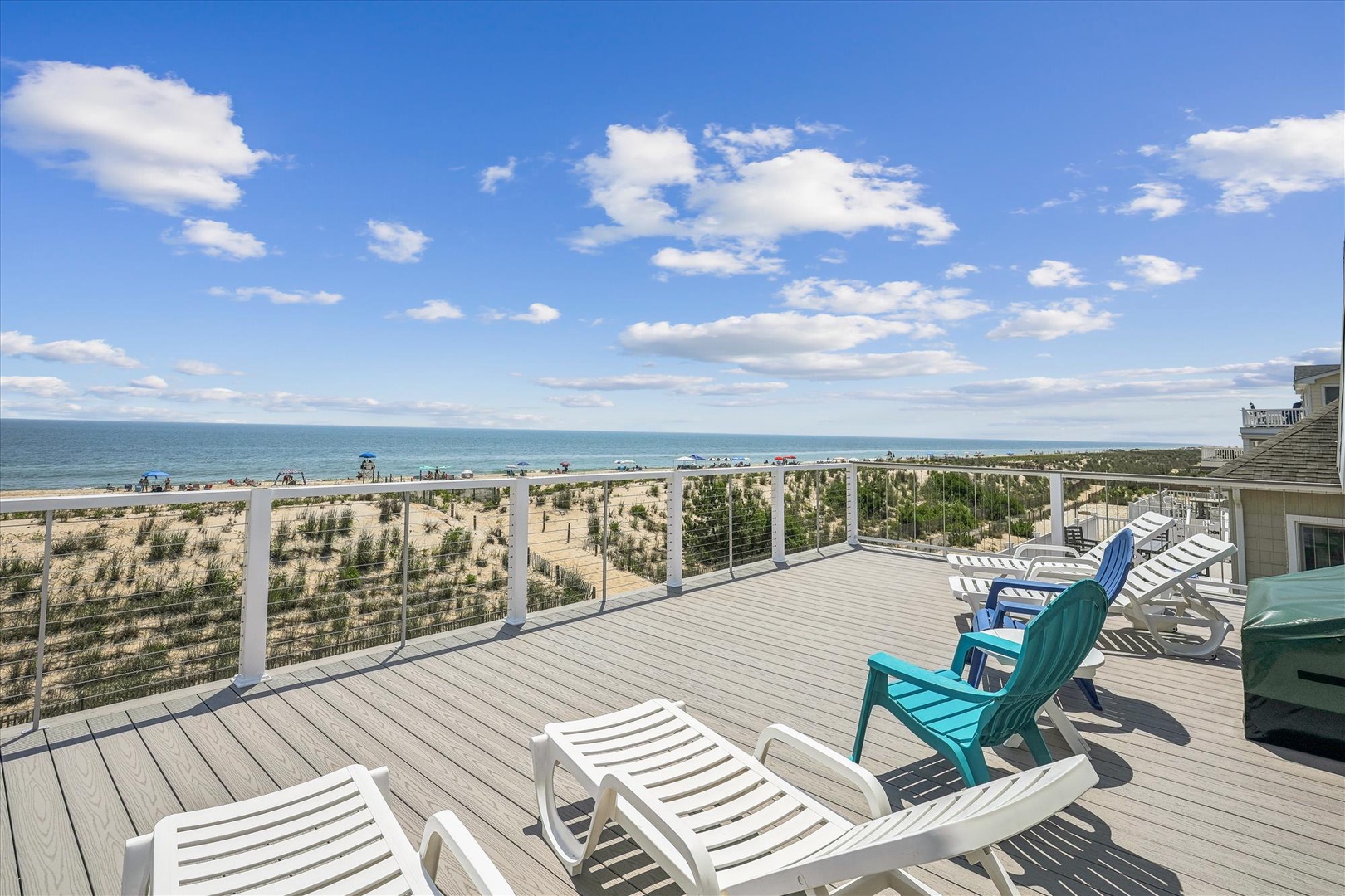 Expansive deck overlooking sandy beach and ocean, featuring lounge chairs and coastal dunes. The property offers direct beach access and panoramic waterfront views. A perfect beachfront location for a seaside getaway.