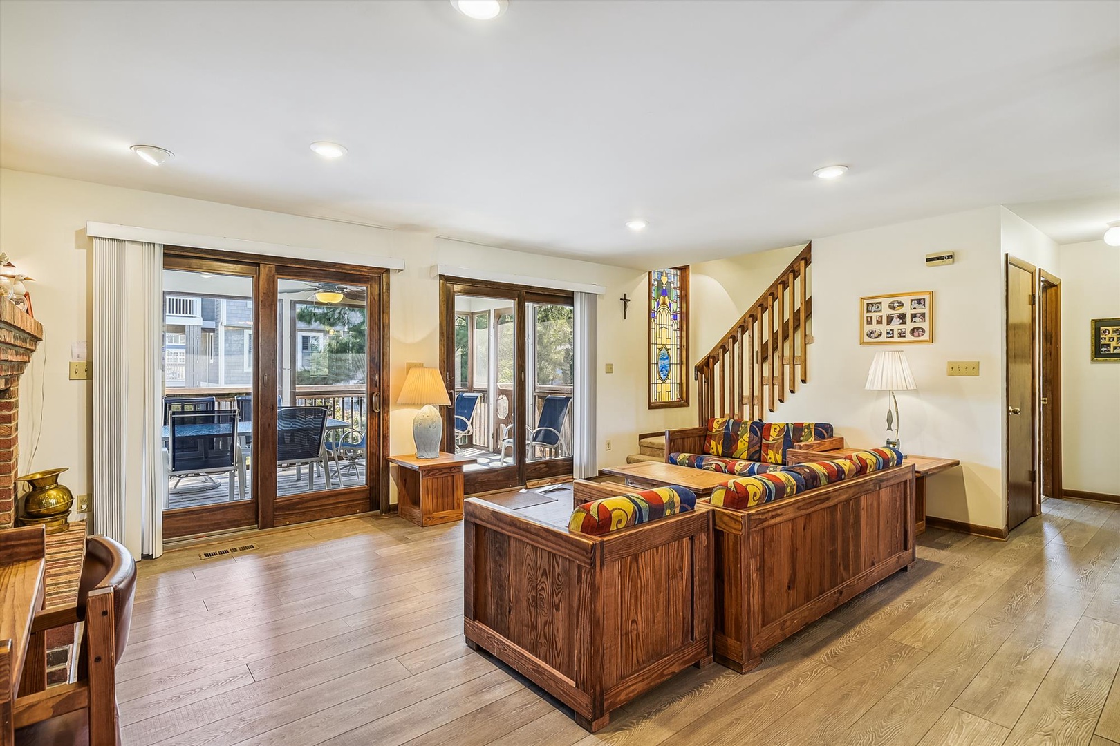 Your spacious living room welcomes you with warm wood tones, colorful seating, and abundant natural light streaming through balcony doors that open to your private outdoor retreat.