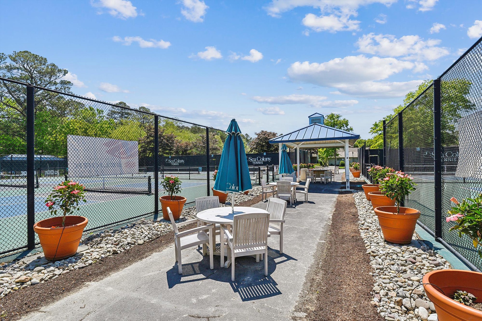 The private tennis court awaits your match, with shaded seating areas and vibrant planters lining the court. Gather under the gazebo or relax courtside as gentle breezes and blue skies set the perfect scene for friendly competition.