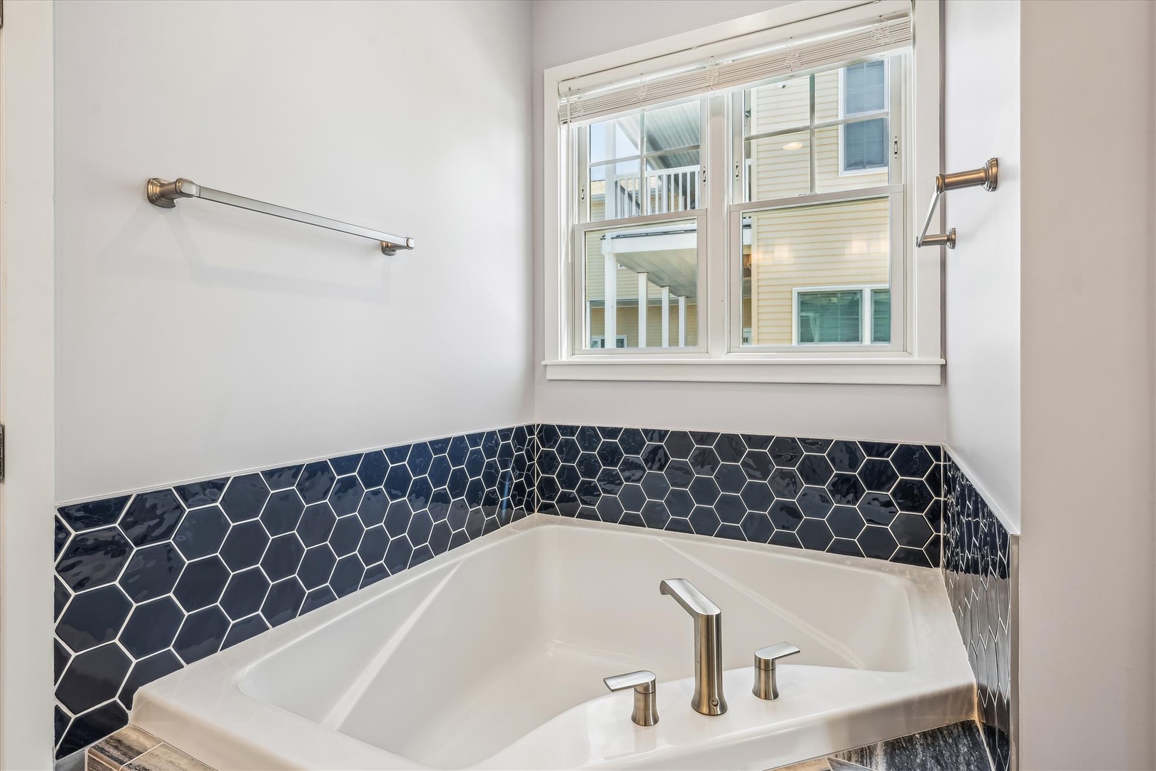 Unwind in your private soaking tub surrounded by elegant navy hexagon tiles and natural light streaming through the window.