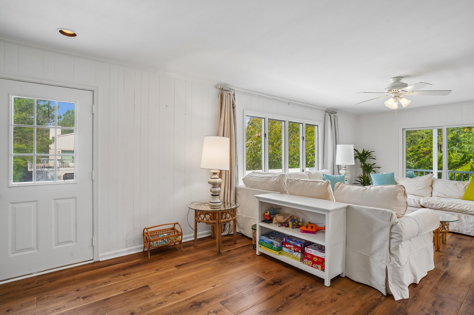 Picture yourself relaxing in this bright, open living room flooded with natural light. Soft cushions invite you to unwind, while games and books keep everyone entertained. Warm wood floors and a coastal vibe welcome you home.
