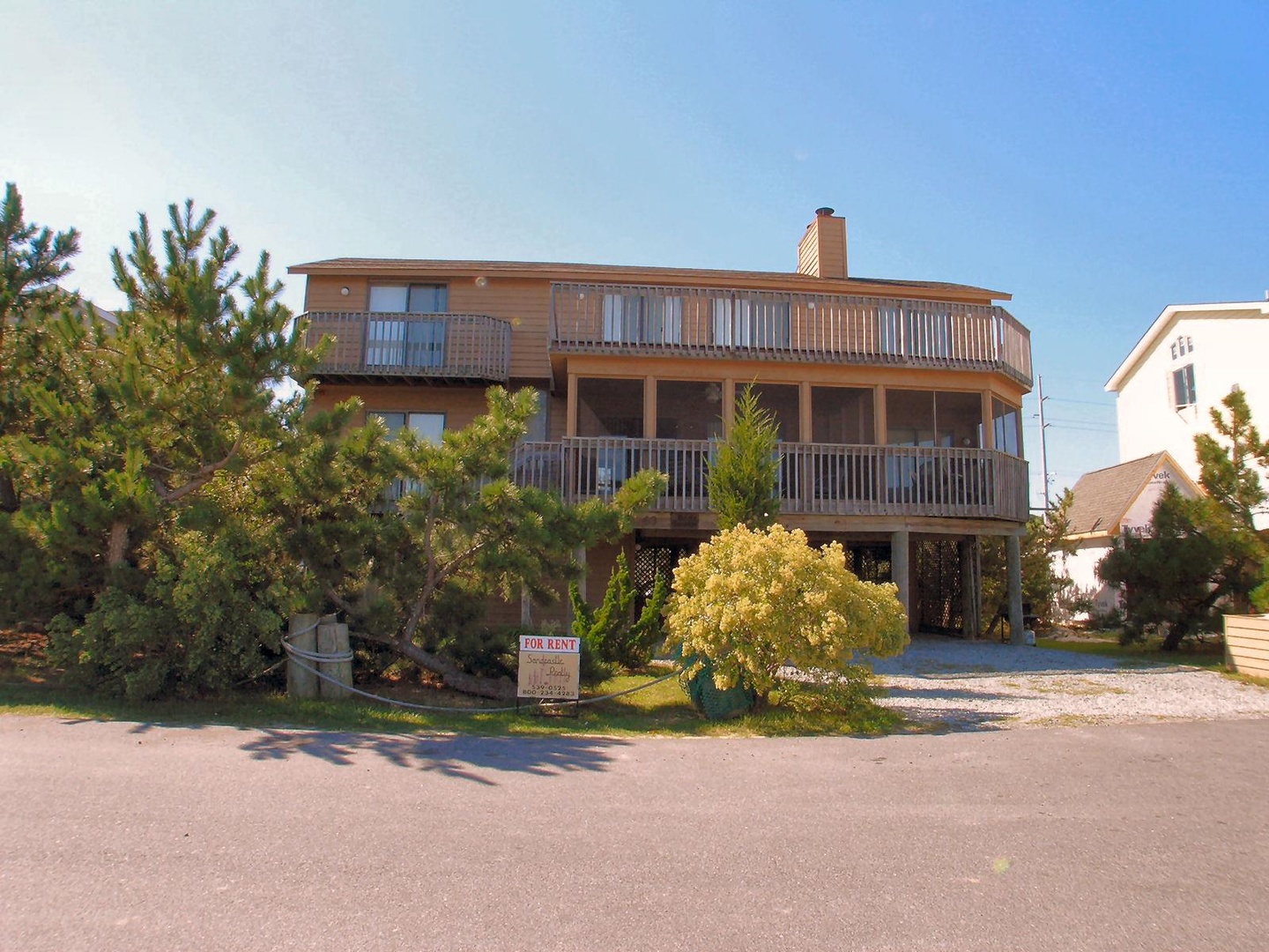 A three-story vacation rental with expansive wraparound balconies offers coastal living in a quiet neighborhood setting, surrounded by mature landscaping and easy beach access.
