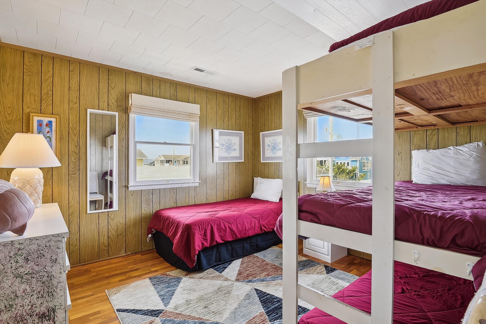 Your cozy beach retreat features bunk beds and a private bedroom, perfect for families. Sunlight streams through the windows, revealing a nearby neighborhood just beyond your coastal getaway.