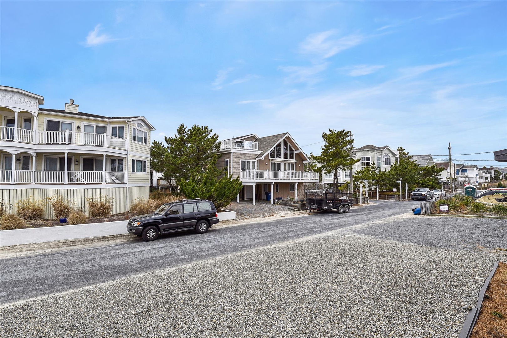 A quiet coastal street where vacation homes line the road, surrounded by natural dunes and coastal greenery, just moments from the beach.