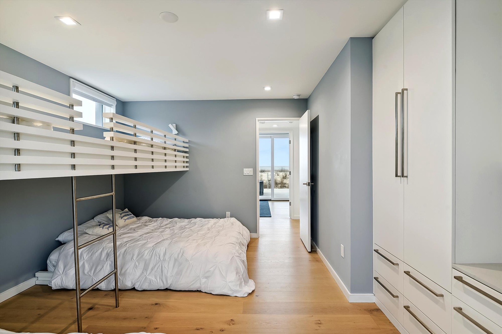 Unwind in this tranquil bedroom featuring a cozy bunk bed, warm hardwood floors, and serene blue-gray walls that wrap you in modern comfort.