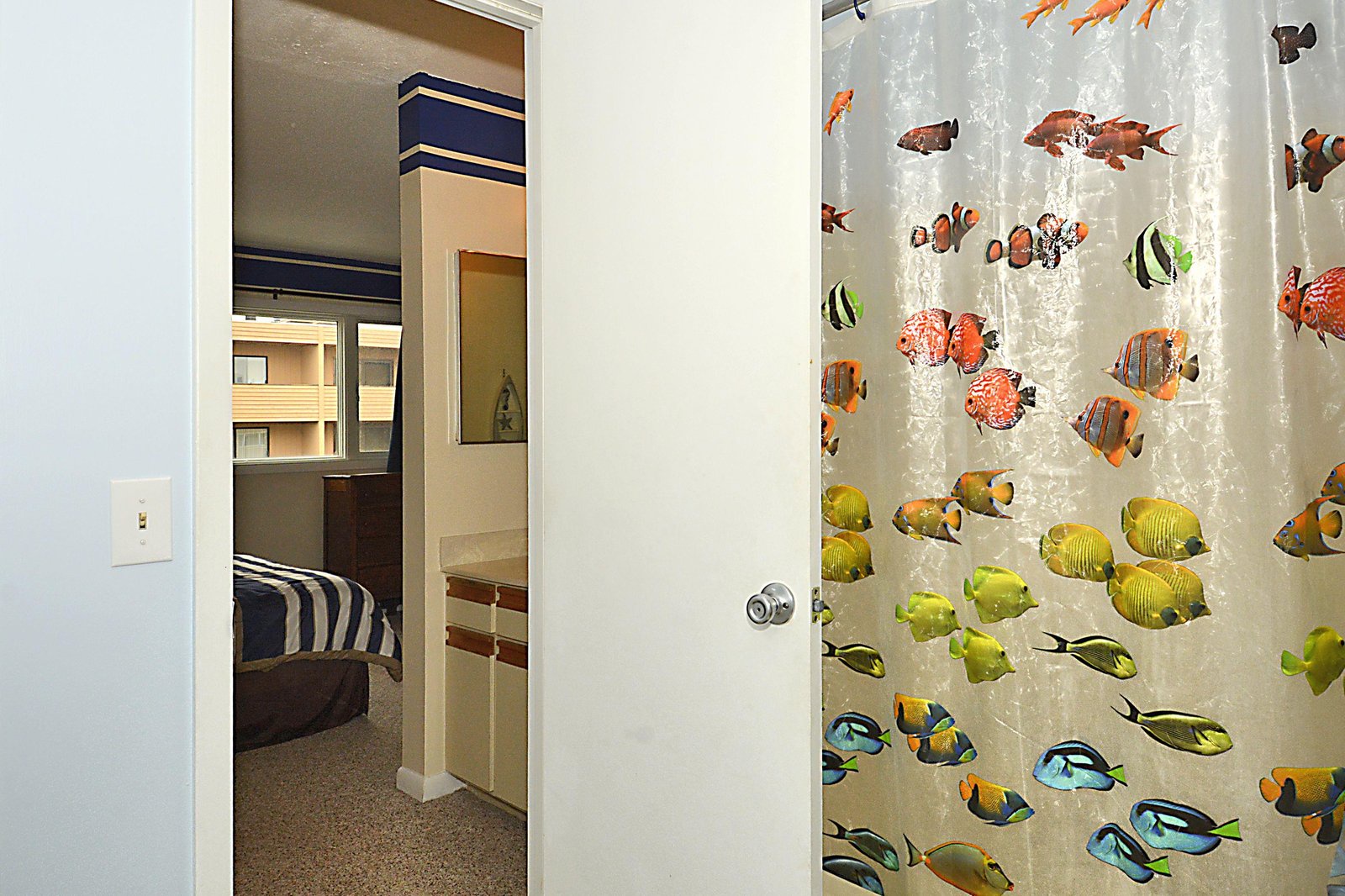 A colorful fish-patterned shower curtain adds a playful touch to your bathroom, with a glimpse through to the bedroom beyond.