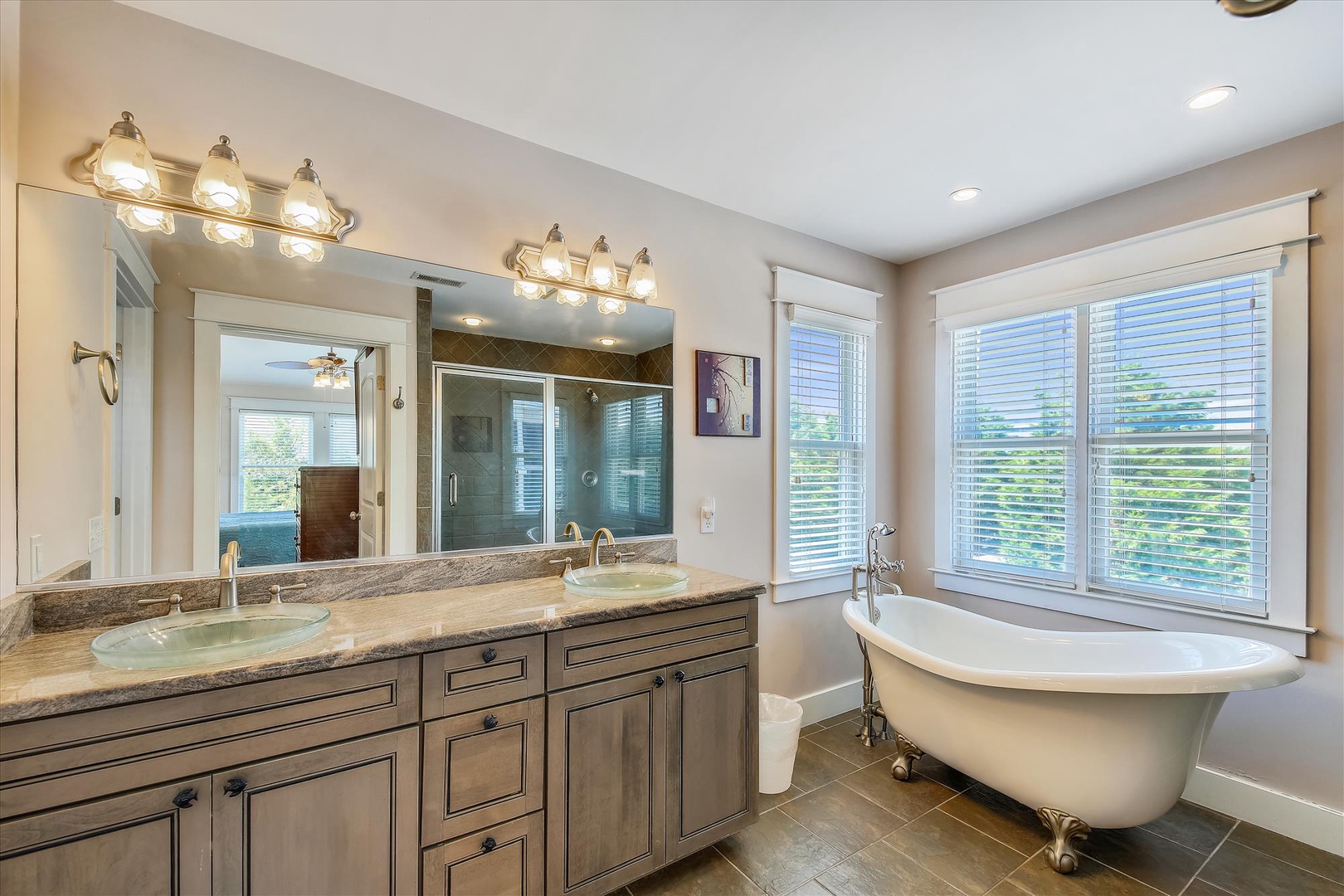 Unwind in your elegant bathroom featuring a luxurious clawfoot tub, dual vanities with granite countertops, and bright natural light from expansive windows.
