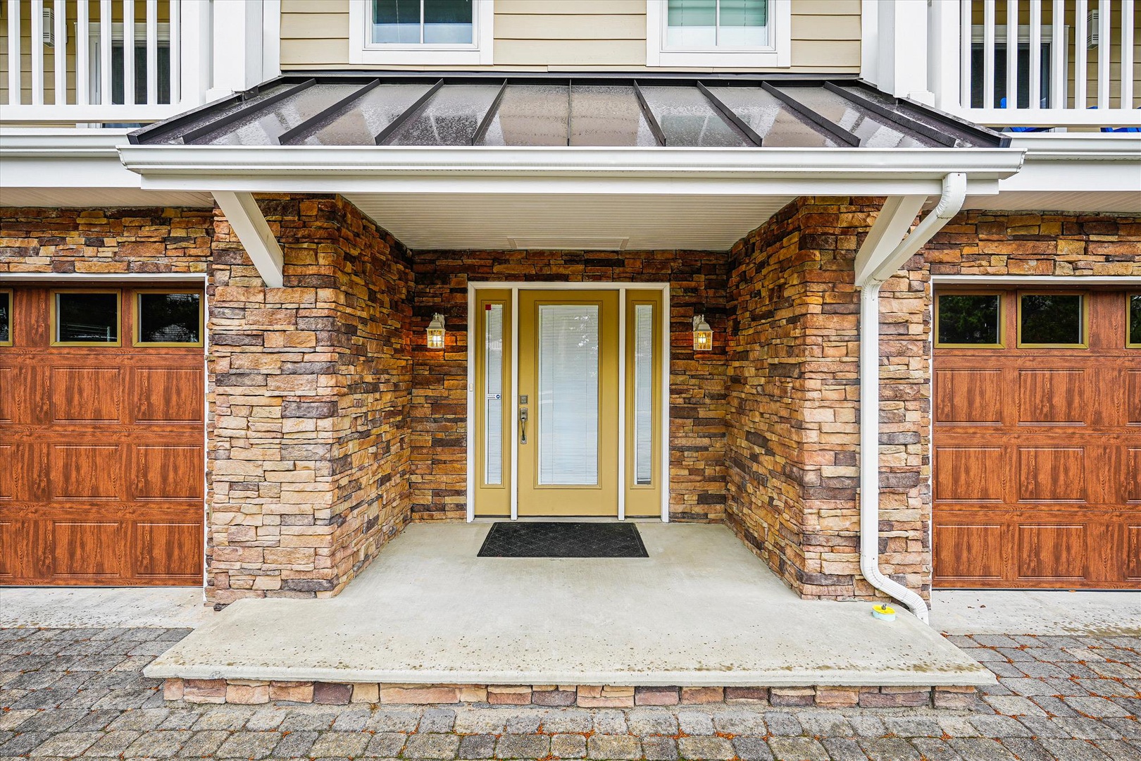 Warm stone archway frames the main entrance with handsome wood garage doors flanking either side, creating a distinctive arrival experience at this property.