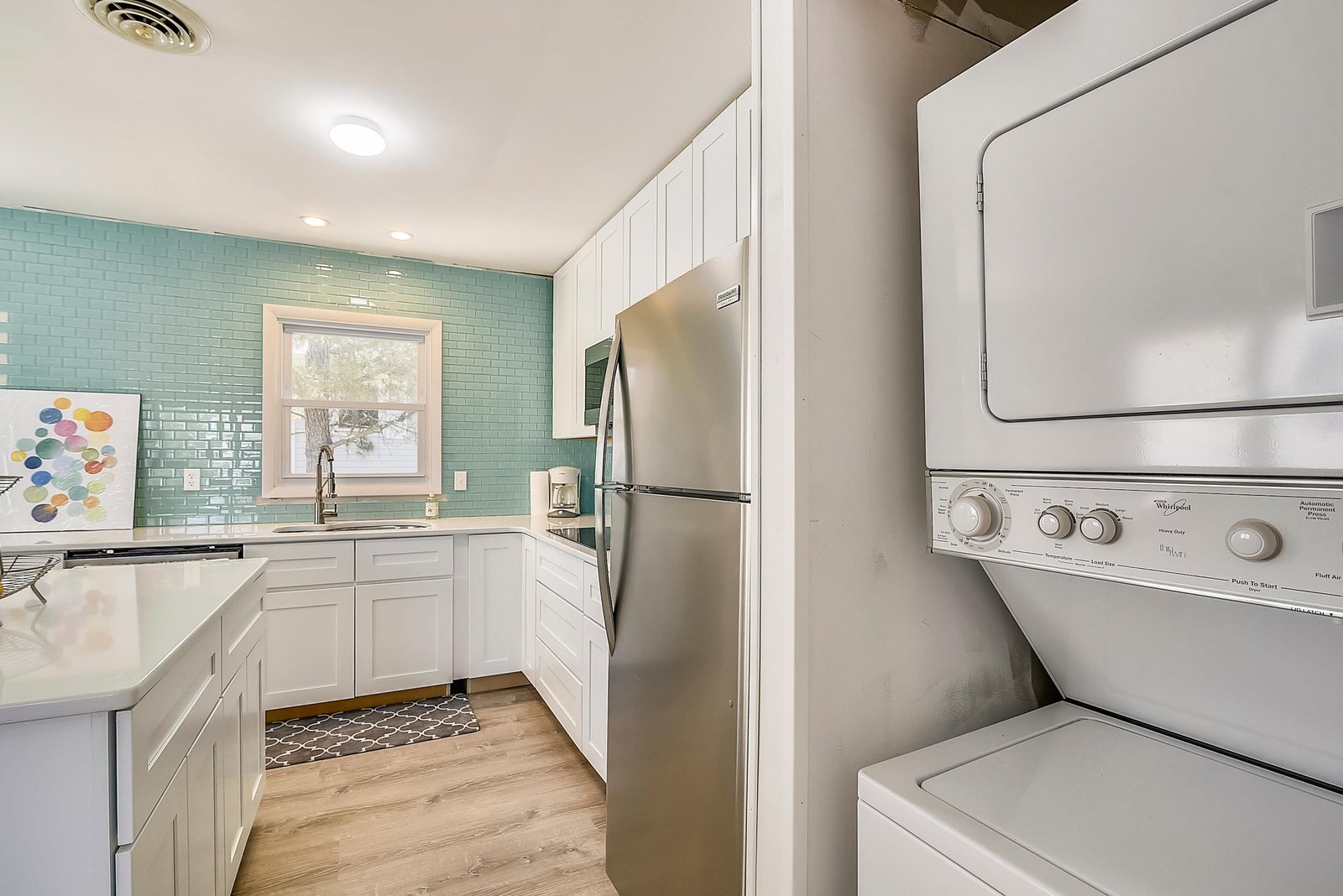 Step into your bright, fully equipped kitchen featuring crisp white cabinetry, soothing aqua tile backsplash, and modern stainless appliances. Convenient in-unit laundry makes your stay effortless.