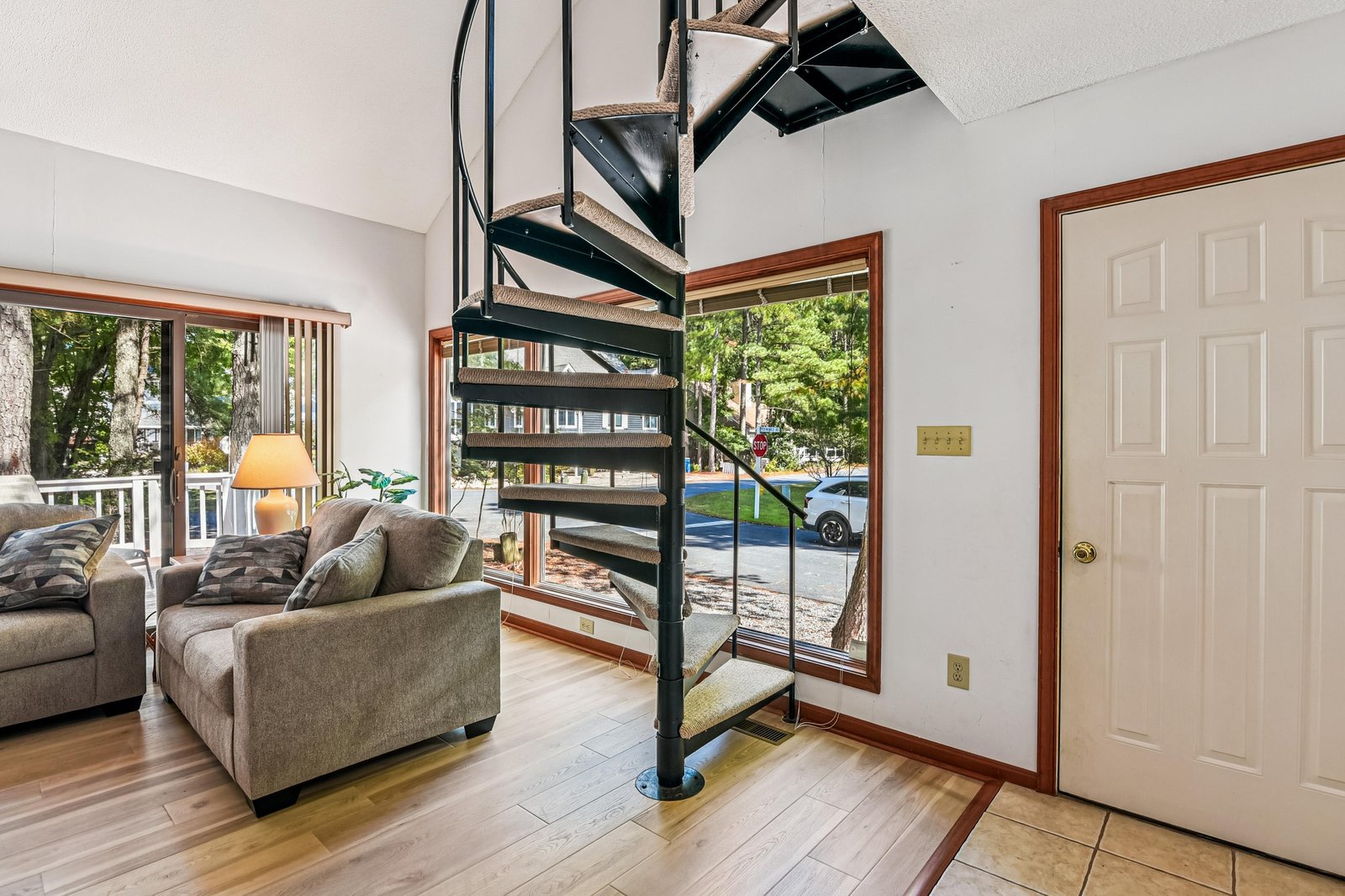Step into a bright, airy living space where a striking spiral staircase connects your world. Large windows frame peaceful neighborhood views, inviting natural light to dance across warm wood floors and plush seating.