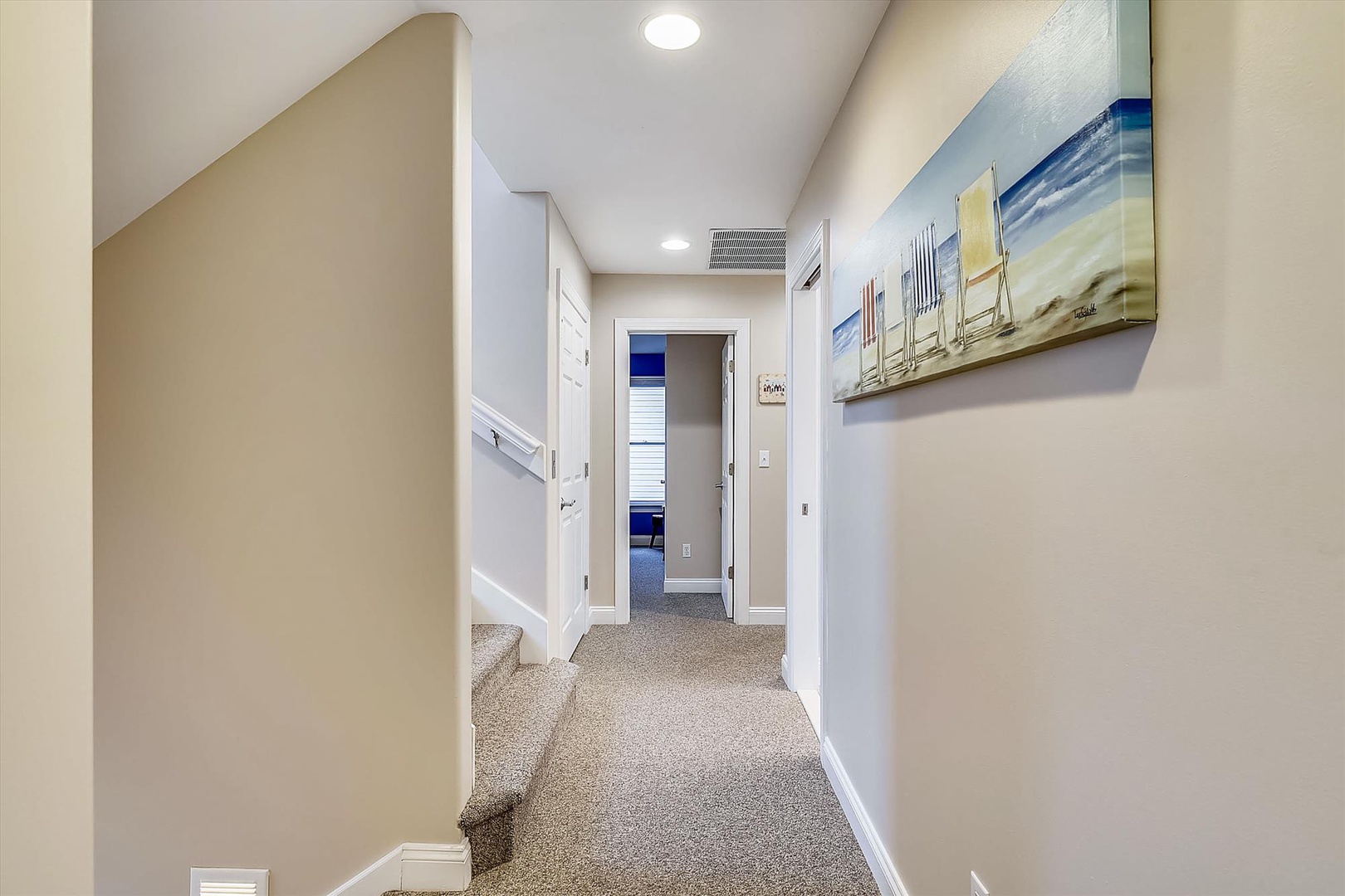 A welcoming hallway connects your private spaces with bright lighting, soft carpeting, and coastal artwork that captures the beachy atmosphere you'll enjoy during your stay.