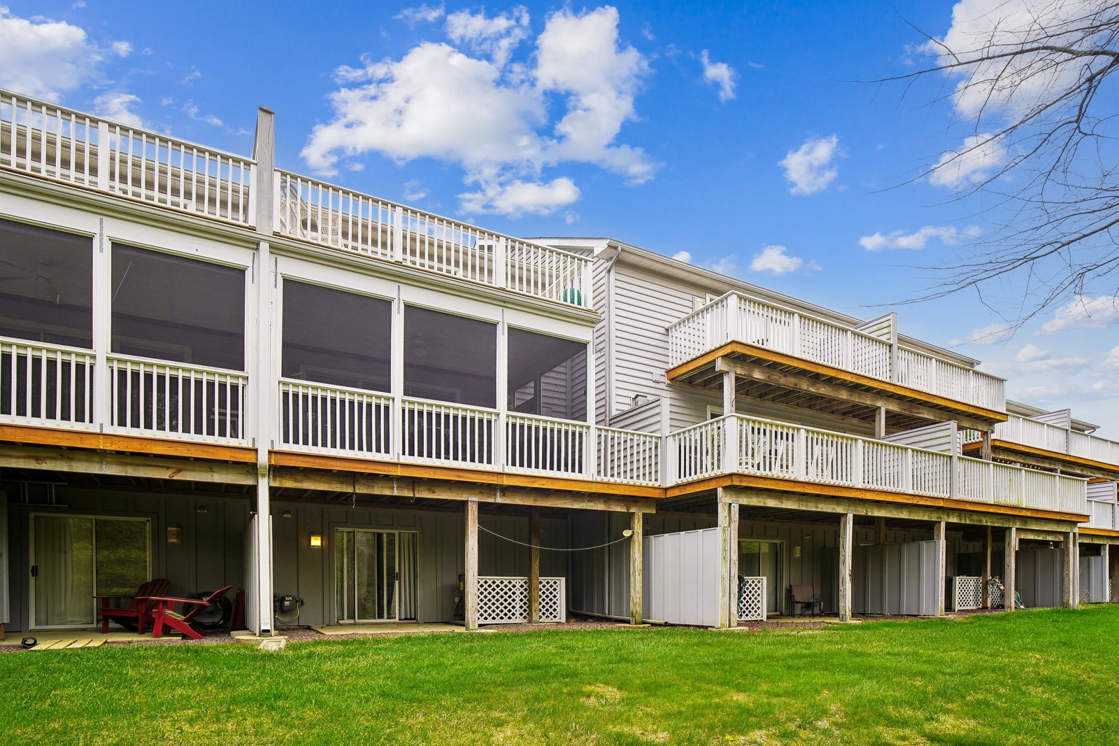 Multi-level vacation property with private ground-floor patios, upper balconies, and spacious lawn areas under bright blue skies—ideal for group getaways or family retreats.