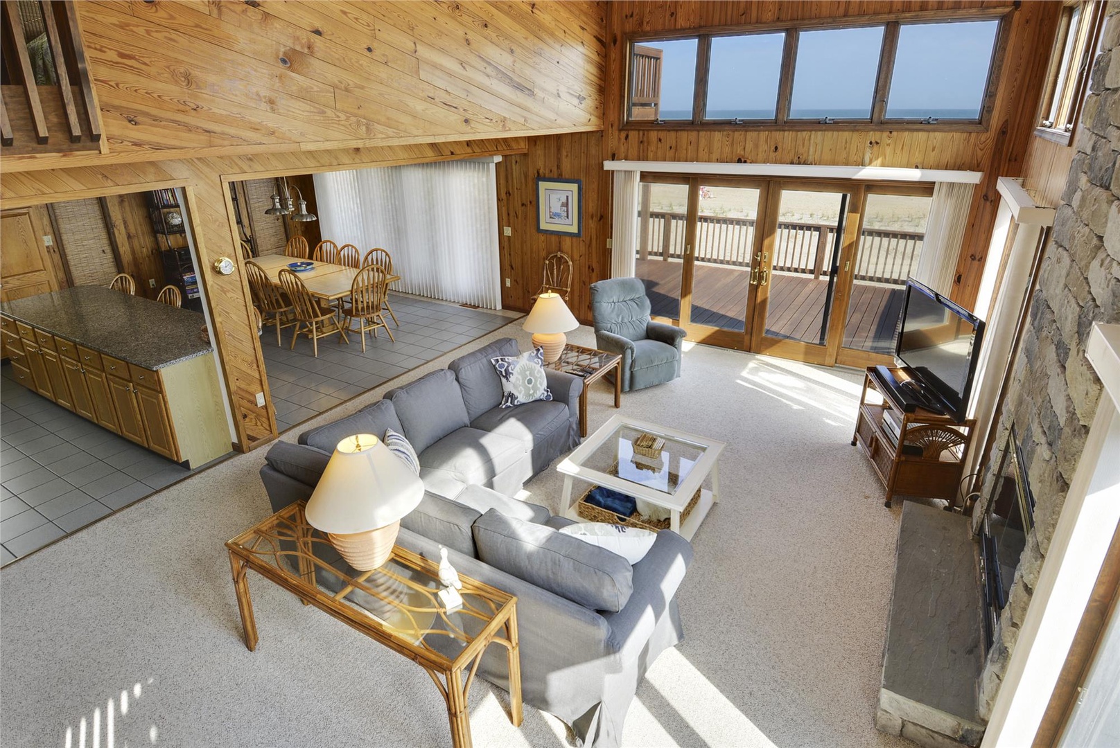 Sunlight streams into the open-concept living space where warm wood walls meet coastal breezes. Relax on the sectional after beach days or gather at the dining table for home-cooked meals in the fully equipped kitchen.