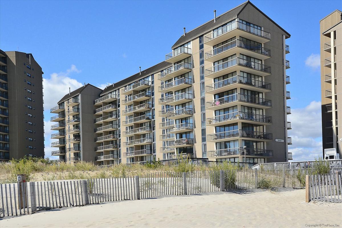 Modern beachfront buildings with private balconies overlook pristine sand and dunes, creating an ideal coastal retreat setting.