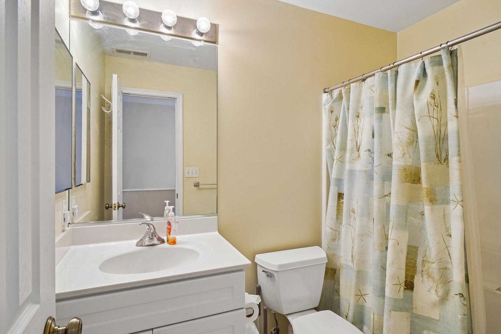 Step into your private bathroom, bright and cheerfully updated with soft yellow walls, crisp white fixtures, and a vanity bathed in warm Hollywood lighting for easy mornings.