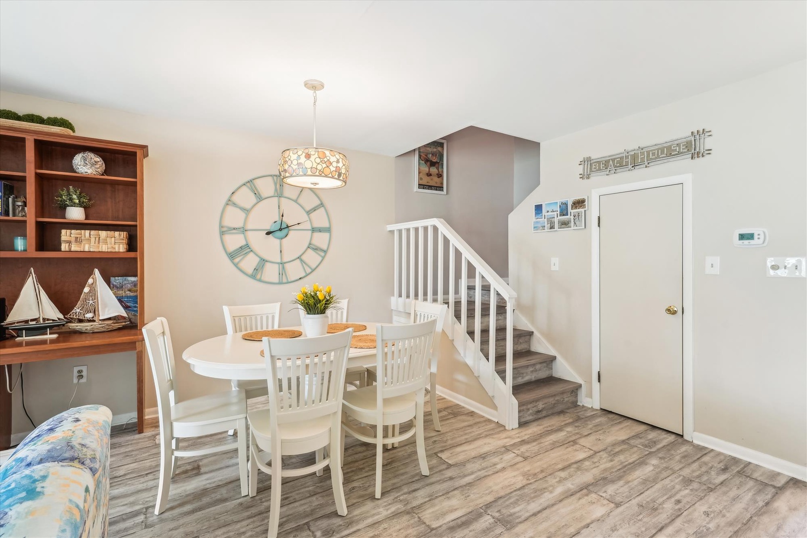 Gather around the inviting dining table where fresh flowers and coastal décor set the scene for memorable meals. A charming clock and nautical accents create a relaxed, homey atmosphere perfect for your getaway.
