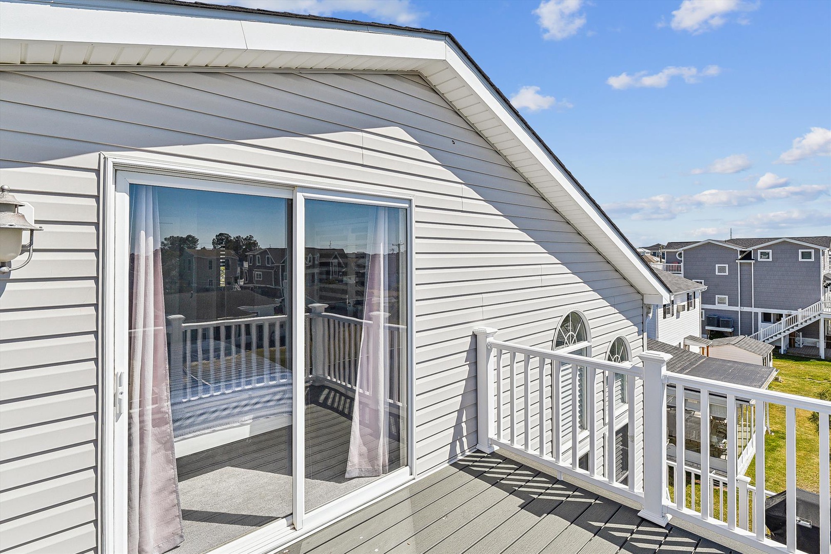 Coastal waterfront property featuring light-colored siding, elevated upper-level balcony with white railings, and neighboring residential buildings visible across the canal.