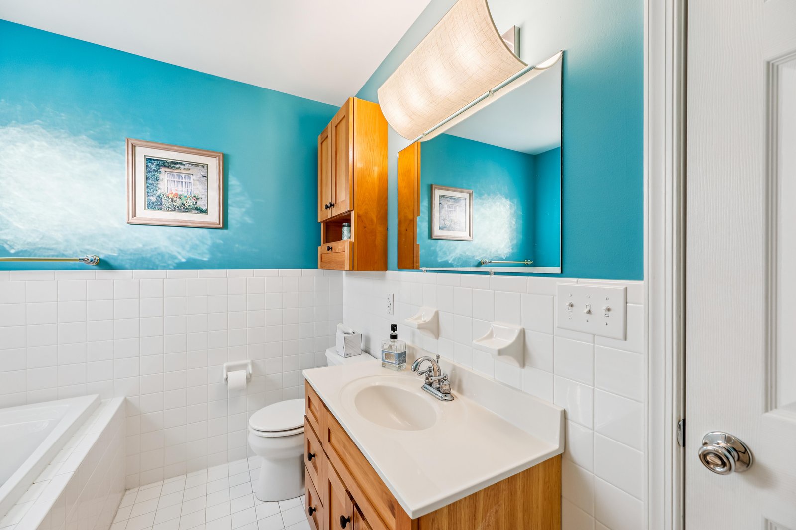 Bright, spacious bathroom with cheerful turquoise walls, classic white tile, and warm wood cabinetry—your perfect spot to refresh after a day of adventure.