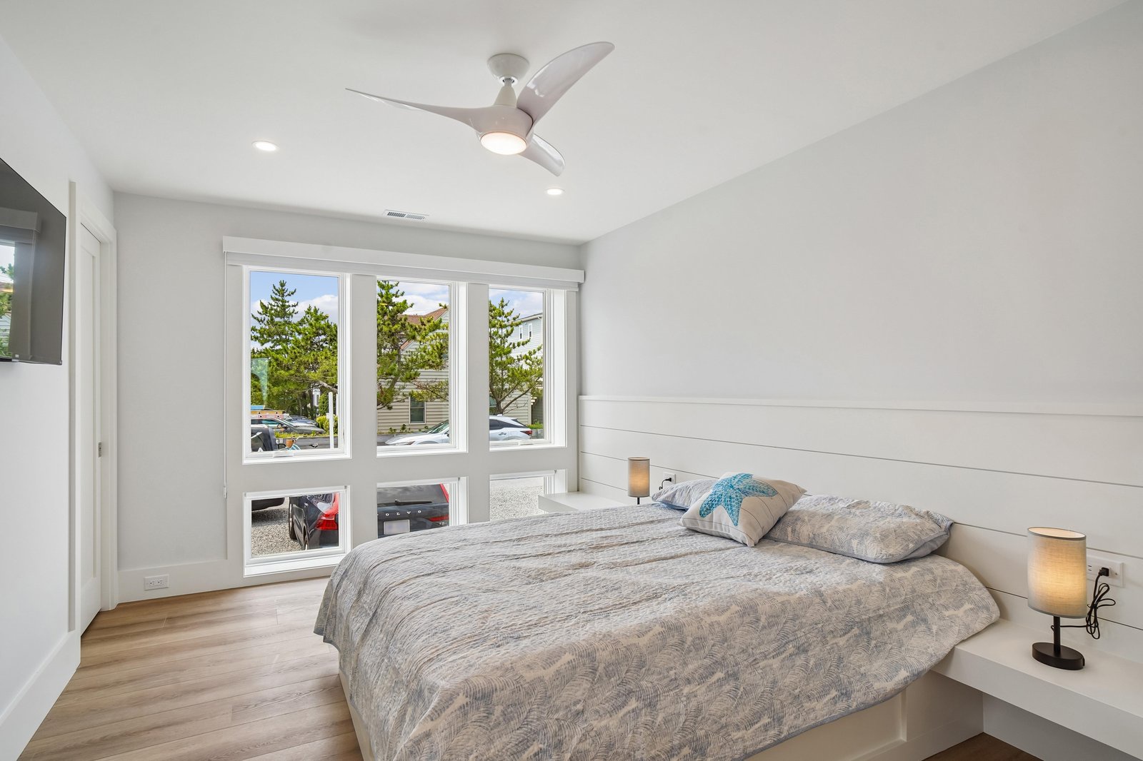 Drift off under soft breezes from your ceiling fan in this serene bedroom, where natural light pours through large windows and clean white accents create a calming retreat.