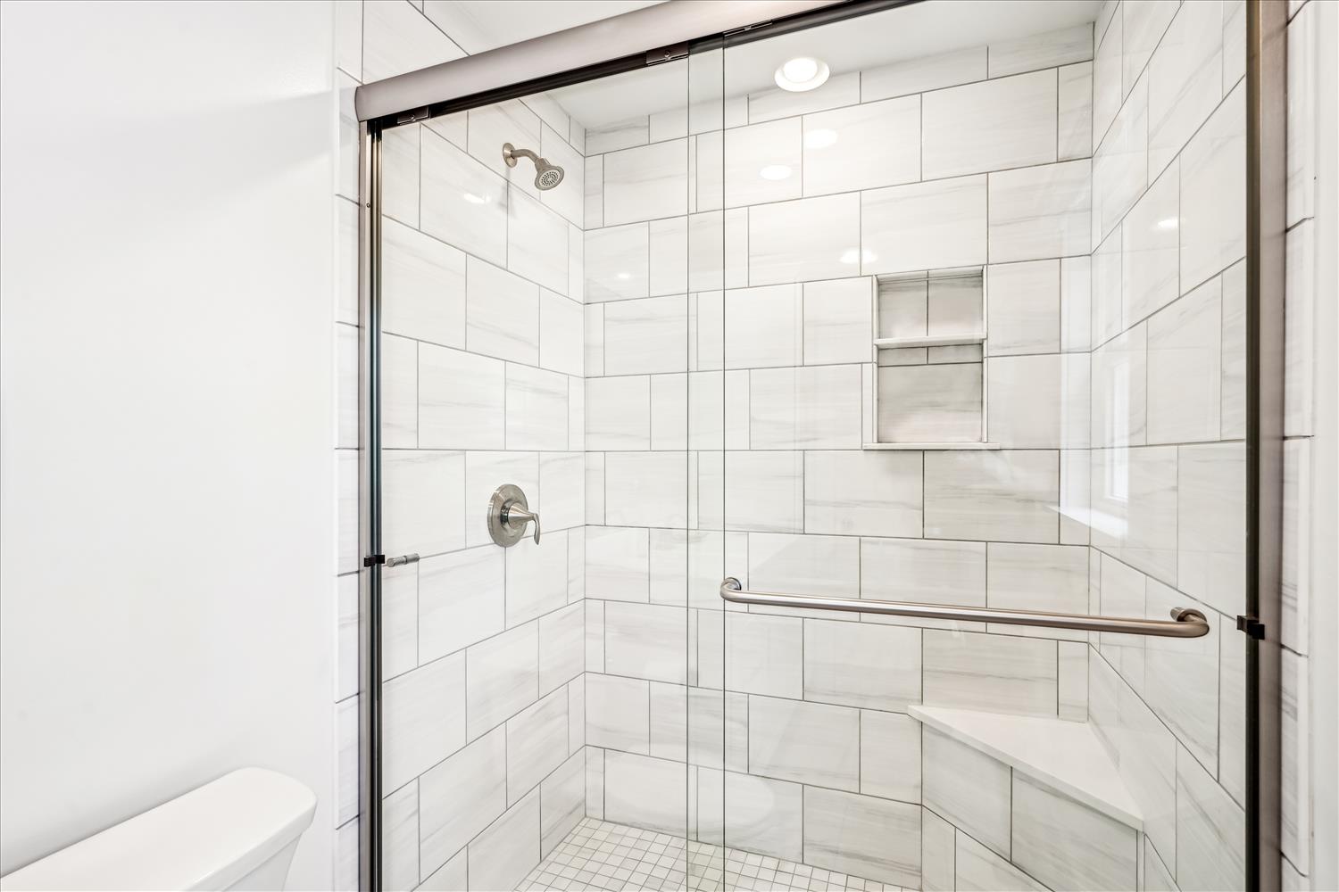 Step into your modern, spotless shower with sleek tile work, built-in storage niche, and a helpful grab bar for safety and comfort.